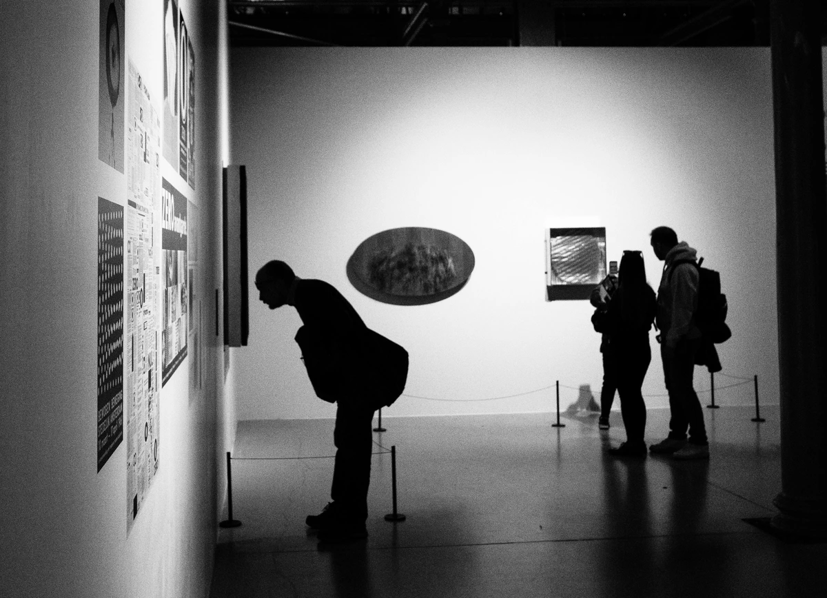 Silhouettes of visitors appreciating contemporary art in a minimalist gallery setting with black-and-white tones.