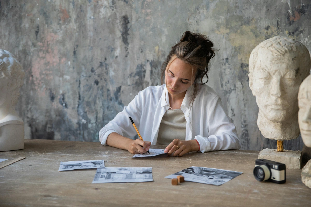 Woman drawing art sketches on paper with vintage tools and realistic style in a professional studio setup.