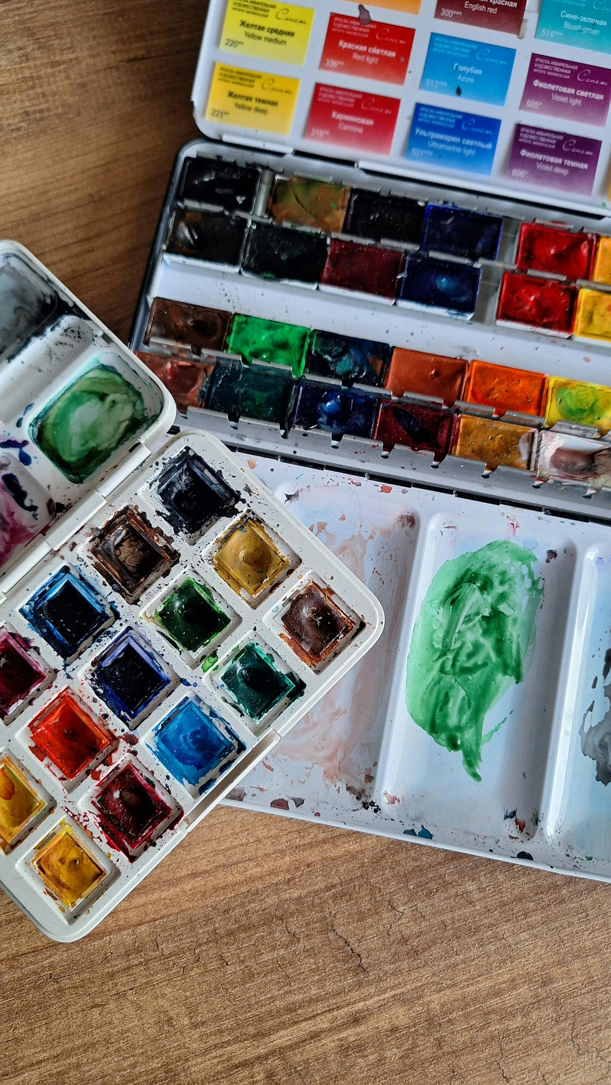 Colorful watercolor palettes arranged on a rustic wooden surface for artistic use