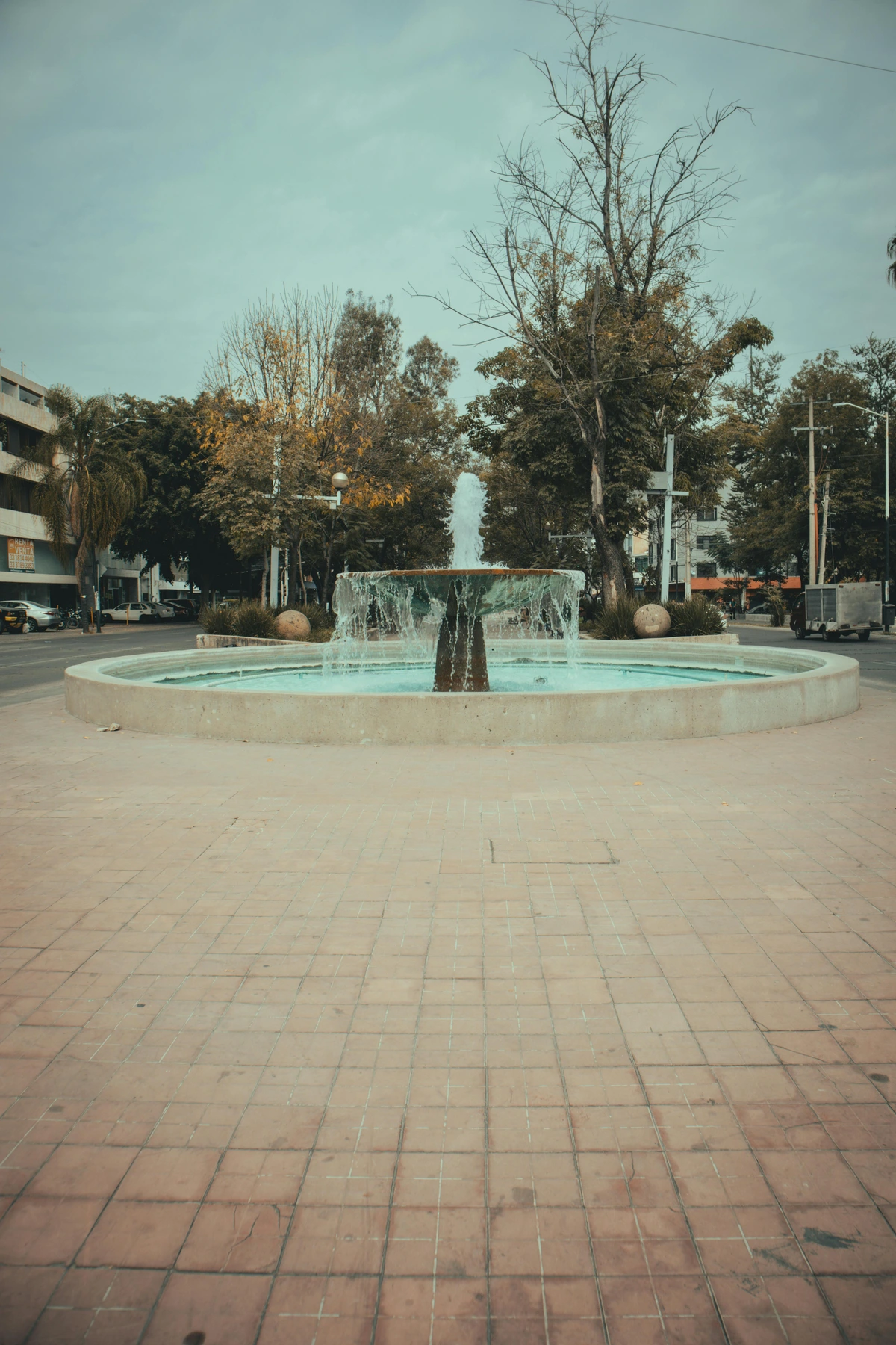 Picturesque fountain on City Square, a symbol of civic pride and community gathering, surrounded by lush trees and stone tiles, available as free stock photo for public use.