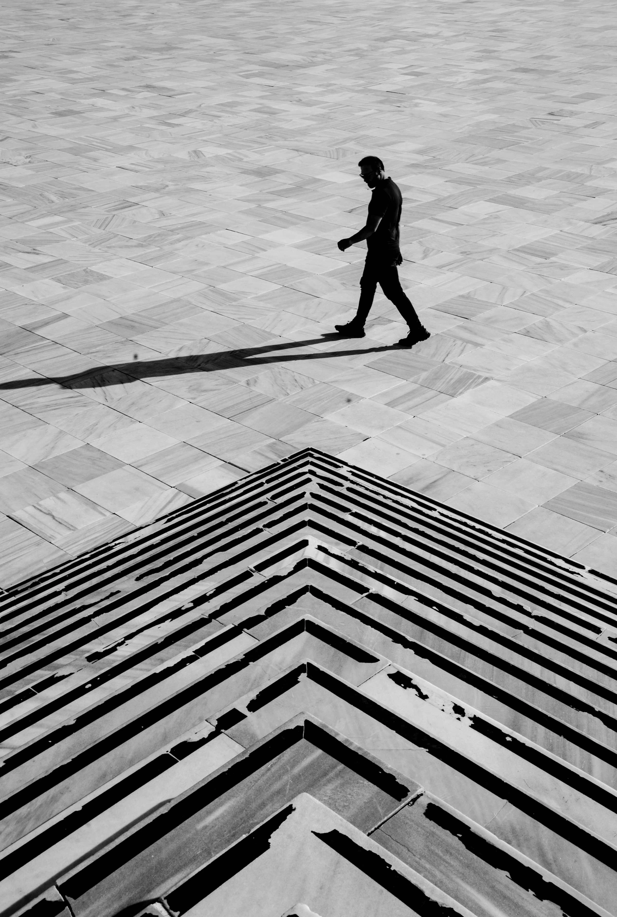Silhouette of a man casting a sharp shadow over a geometrically patterned hardwood floor in a minimalist urban setting.