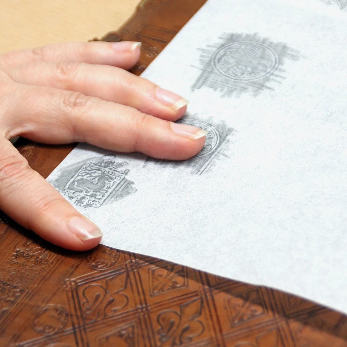 Close-up of a hand performing frottage on an embossed leather surface, transferring the texture onto paper.