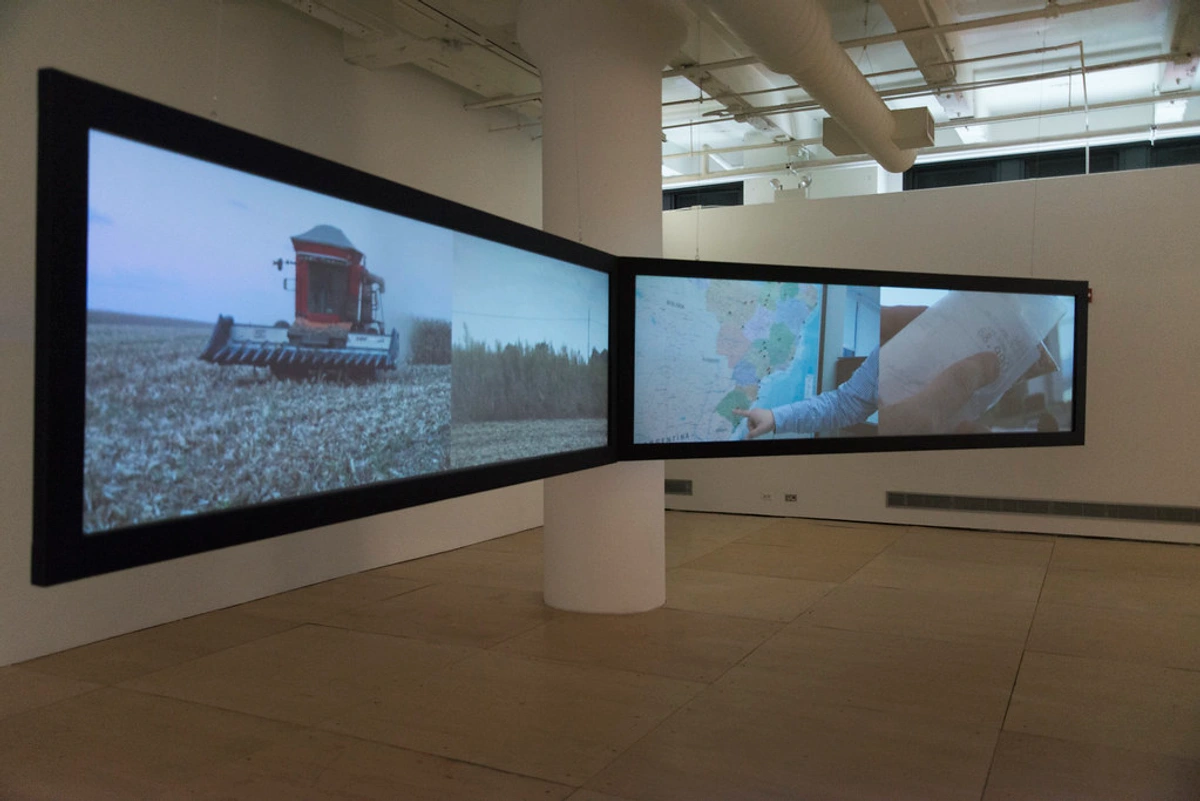 Multi-screen video installation showing a combine harvester in a field and a map of South America with a hand pointing to a region.