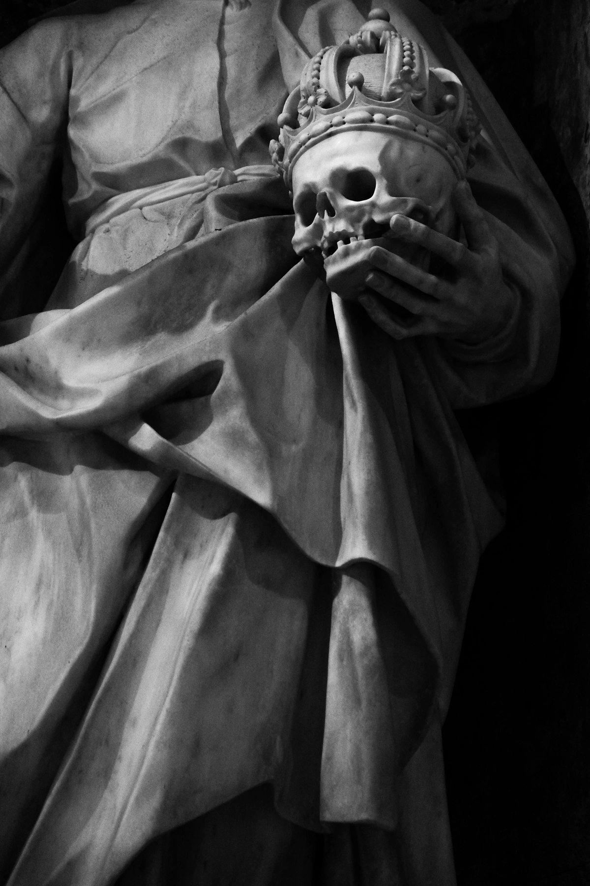 Royal figure holding ornate skull with crown, symbolizing memento mori art in a black and white studio setting.