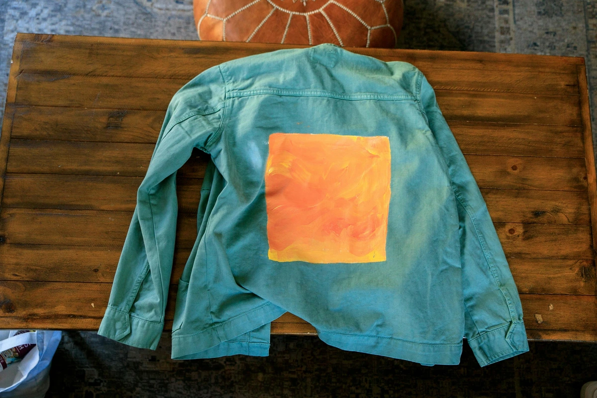 A turquoise jacket with an orange abstract square design on a rustic wooden table, free stock photo.