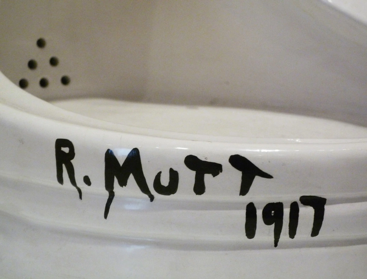 A urinal artwork by Marcel Duchamp labeled 'R. Mutt 1917', presented as a provocative readymade art piece challenging traditional art conventions, signed by the artist in black paint on a white ceramic surface.