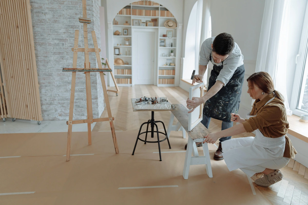 A man demonstrates how to frame a canvas to a woman in an art studio.