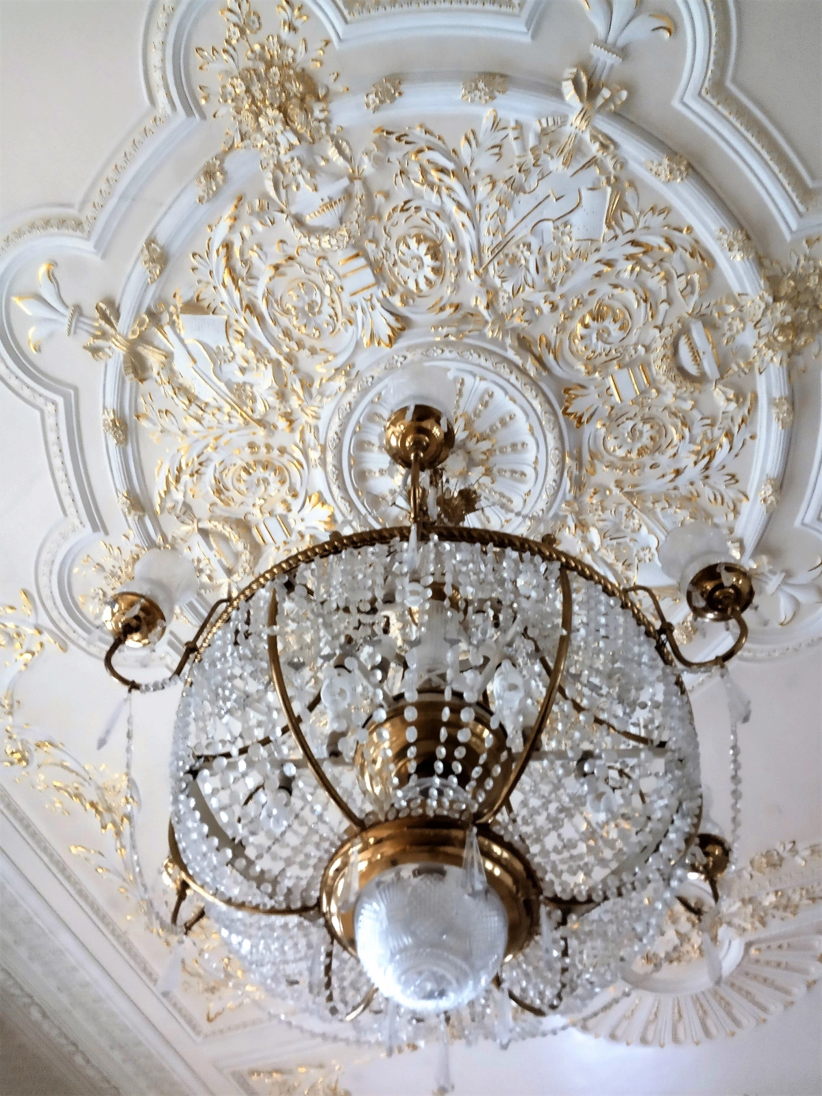 Ornate Rococo hall interior decoration with a crystal chandelier and gilded plasterwork.