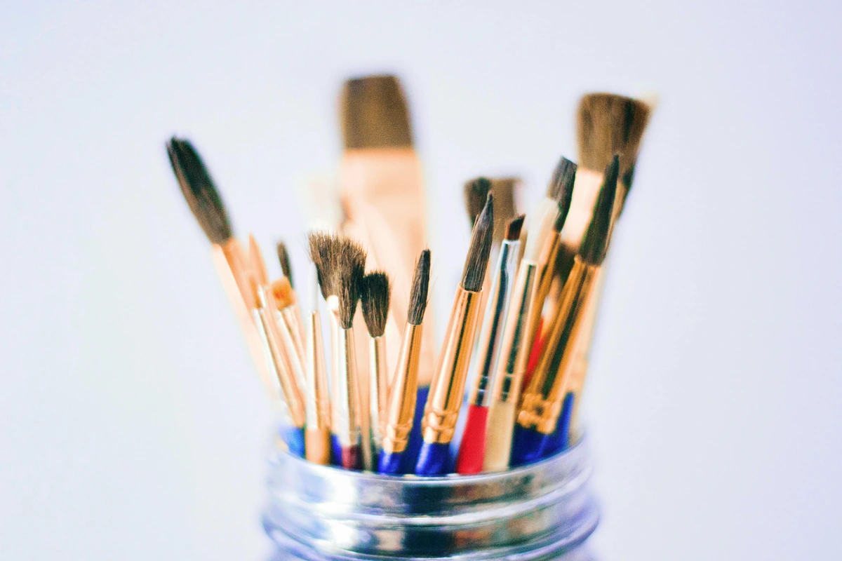 Shallow photography of various paint brushes in a jar with a metal rim, some with blue and red handles.