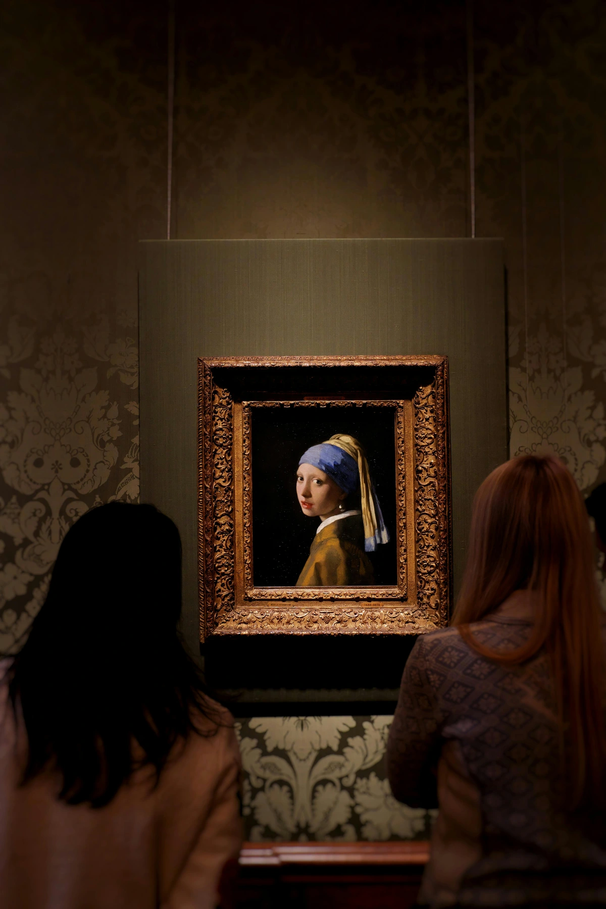 Tourists admiring Johannes Vermeer's 'Girl with a Pearl Earring' painting in a museum gallery.