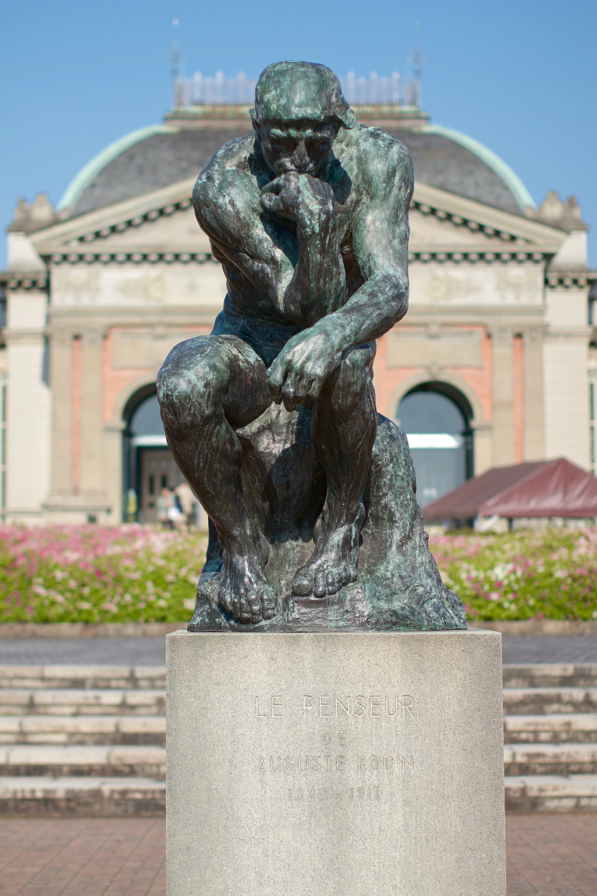 The Thinker sculpture by Auguste Rodin, a bronze statue in a contemplative pose on a stone pedestal.