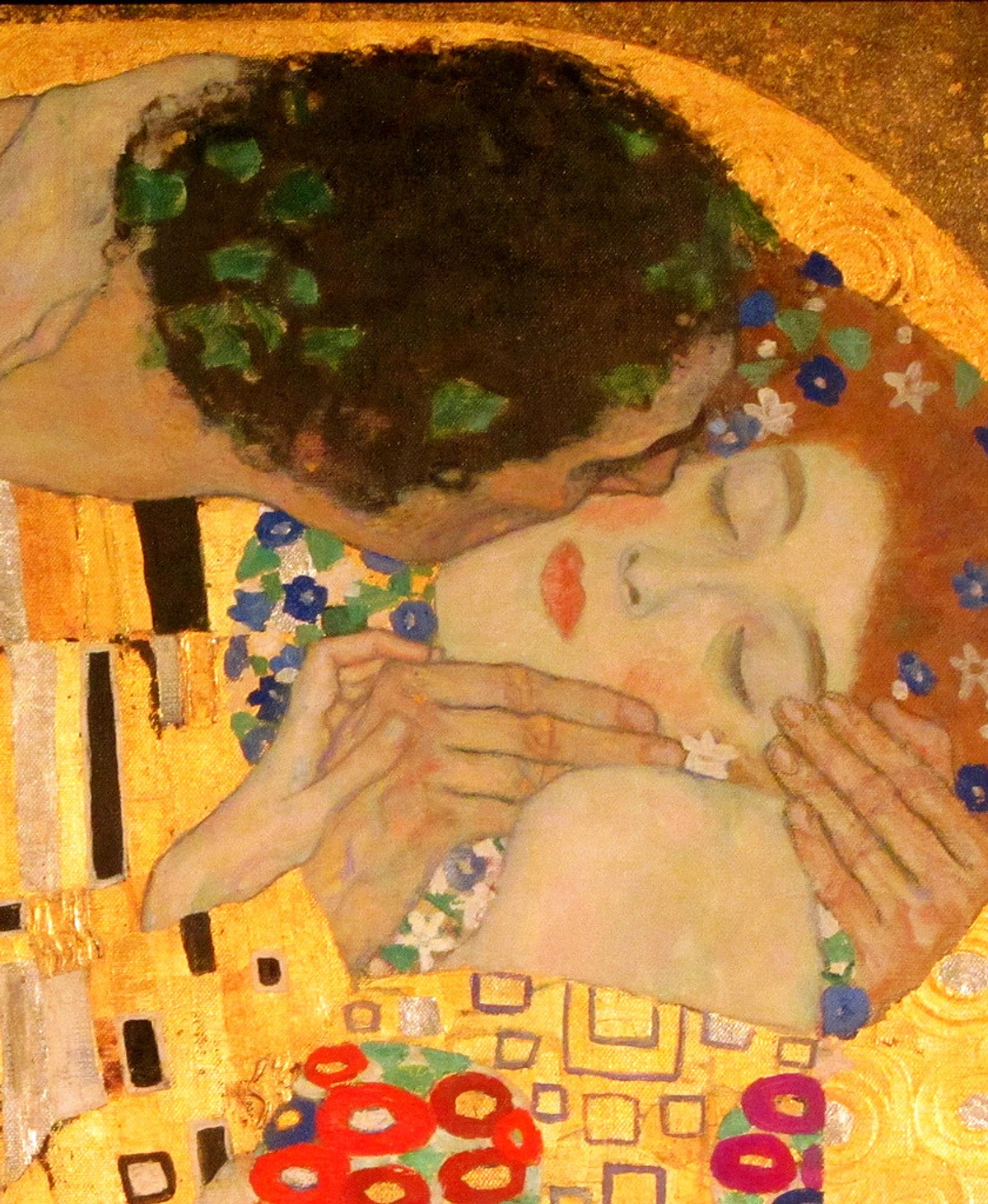Detail from Gustav Klimt's 'The Kiss', showing an embracing couple adorned with gold leaf and floral patterns.