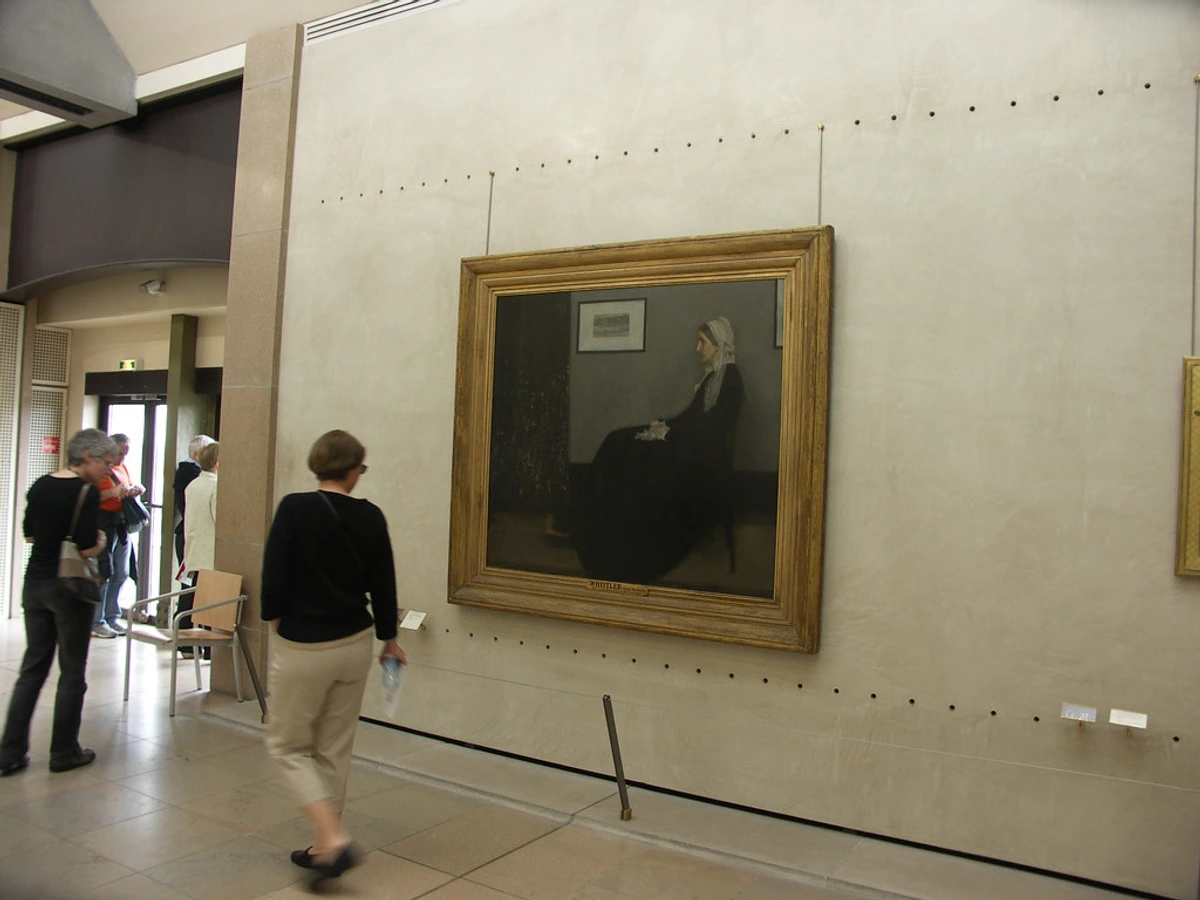 Whistler's Mother painting displayed at the Orsay Museum in Paris, with visitors in the foreground.