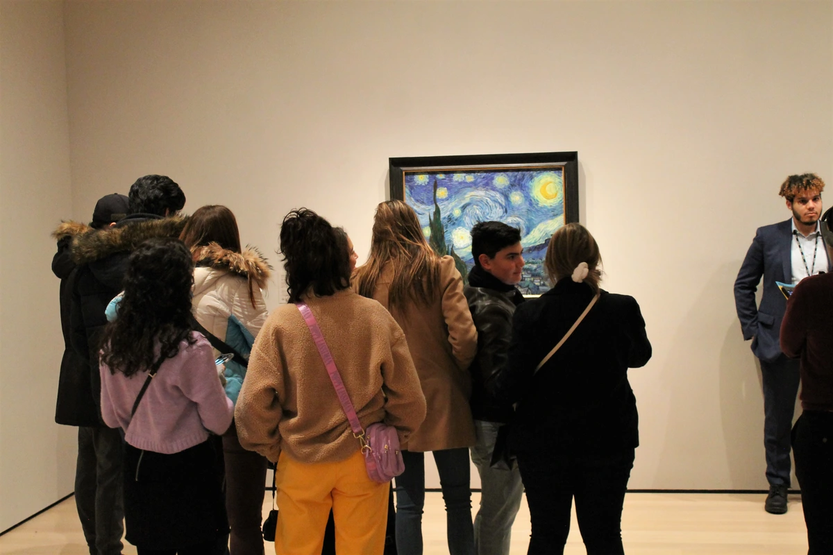 A diverse crowd of people admire Vincent van Gogh's 'The Starry Night' painting in a museum setting.