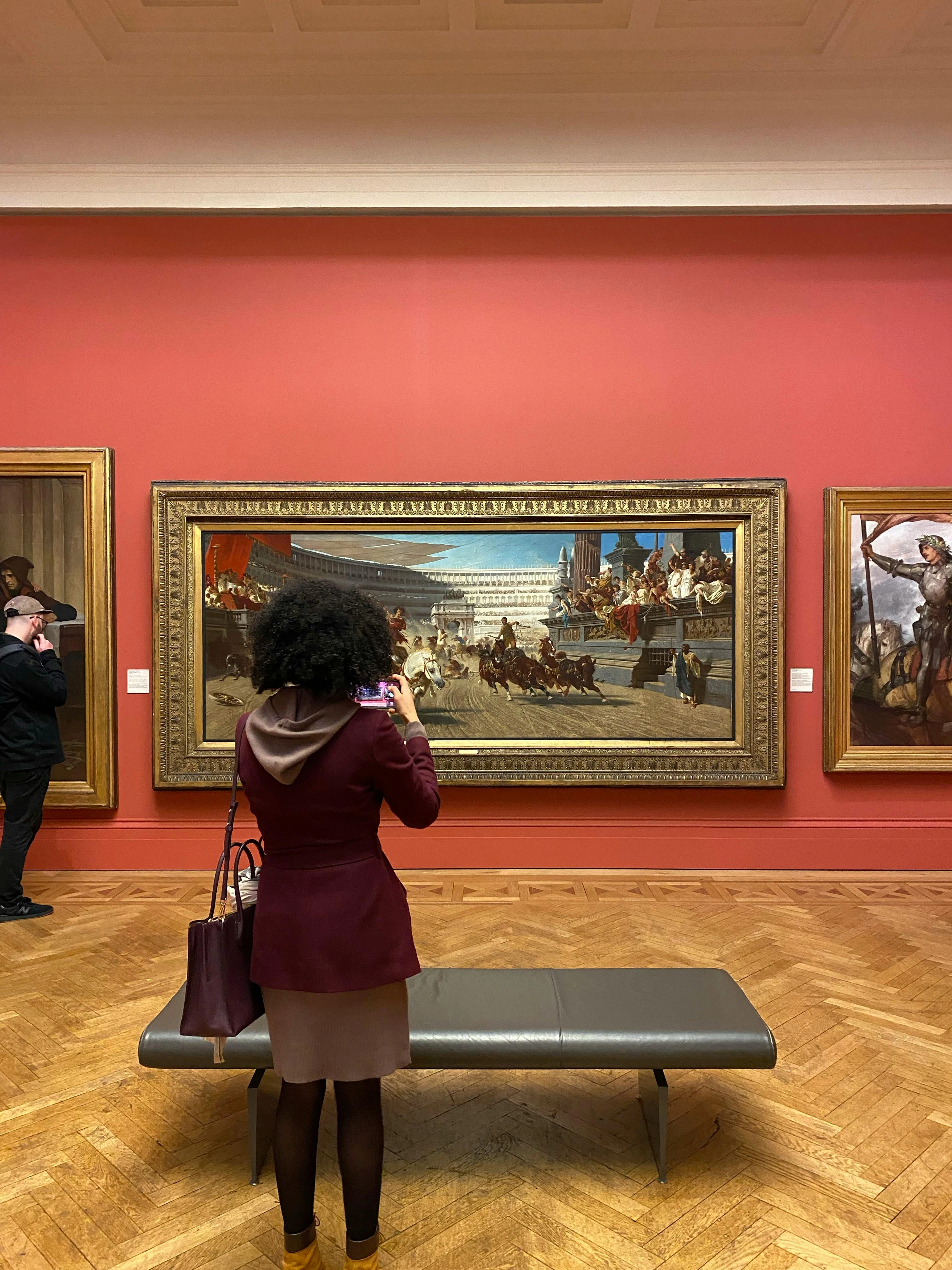 Woman comprehending artwork in museum environment, examining canvas details with smartphone camera, learning from historical artistry in grand gallery space with classical paintings displayed