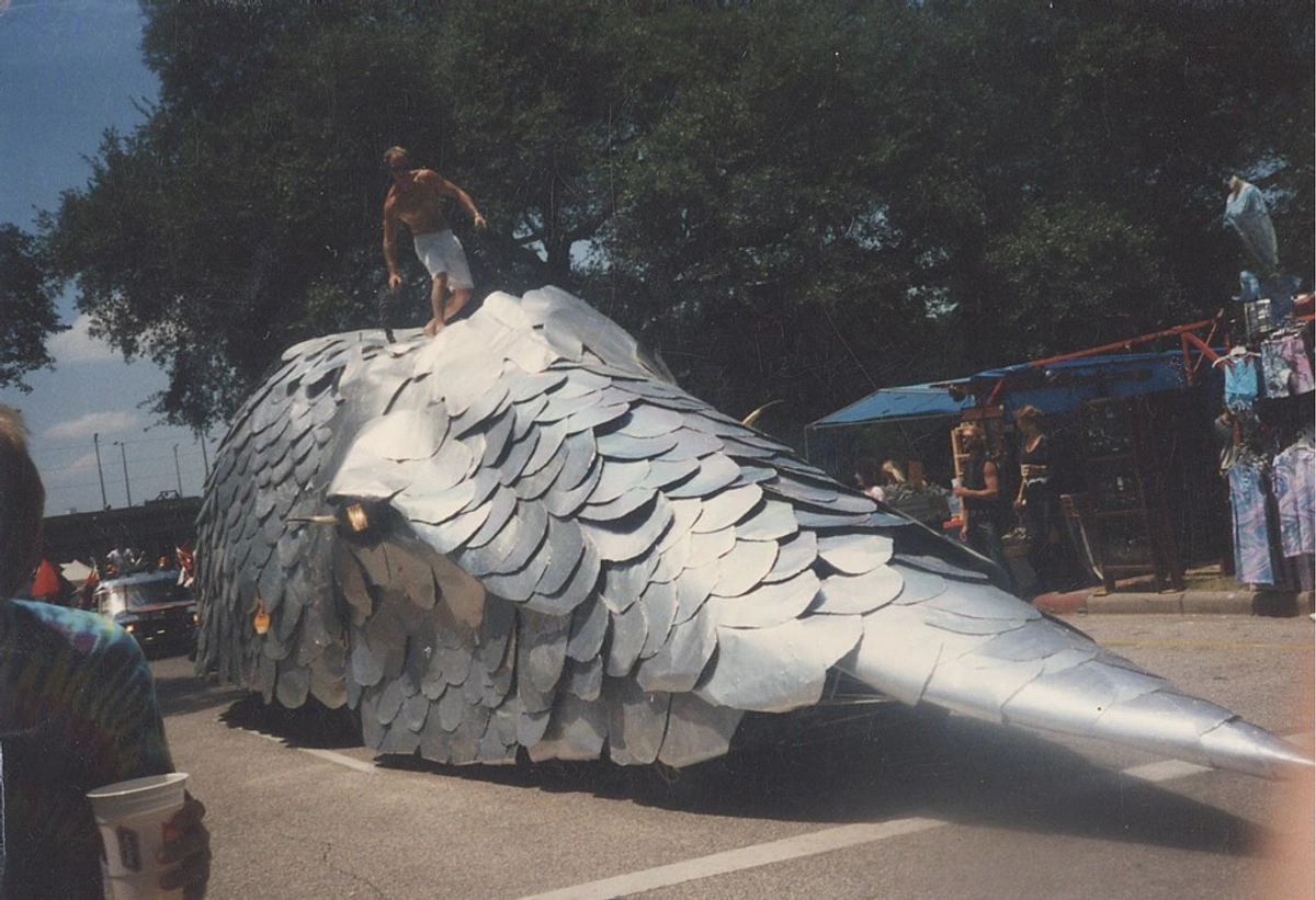 Mark Bradford's colossal carmadillo float in a parade, covered in metallic scales with a performer on top.