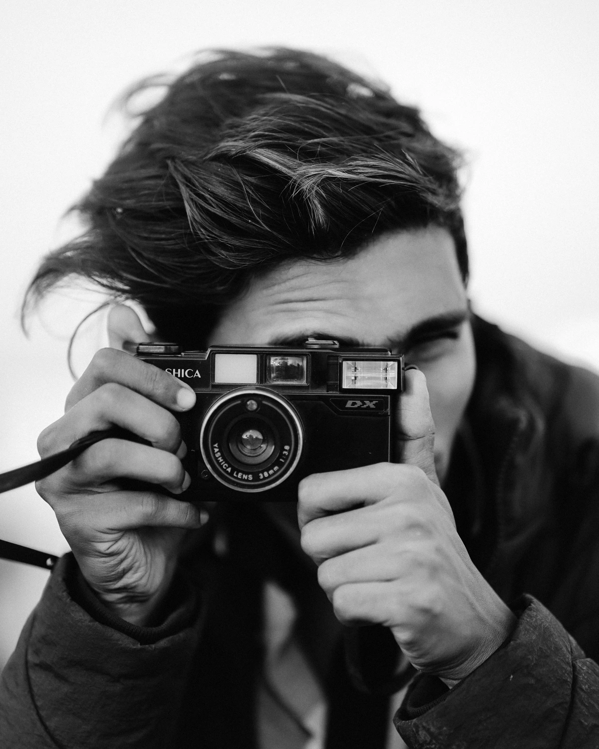 Black and white close-up of a young man holding an analog camera to his eye, ready to take a photo.