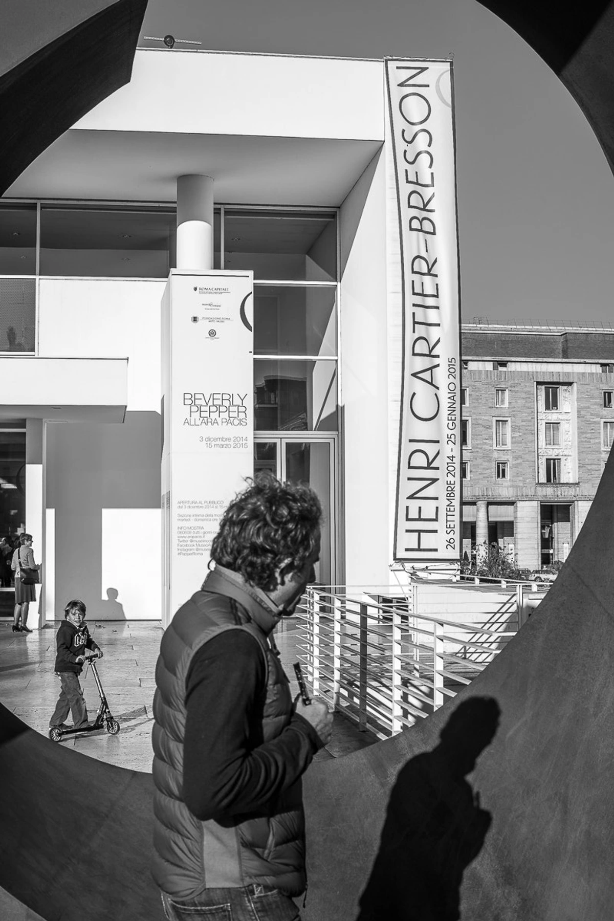 Henri Cartier-Bresson exhibition banner outside a modern building, with people and a child on a scooter in the foreground.