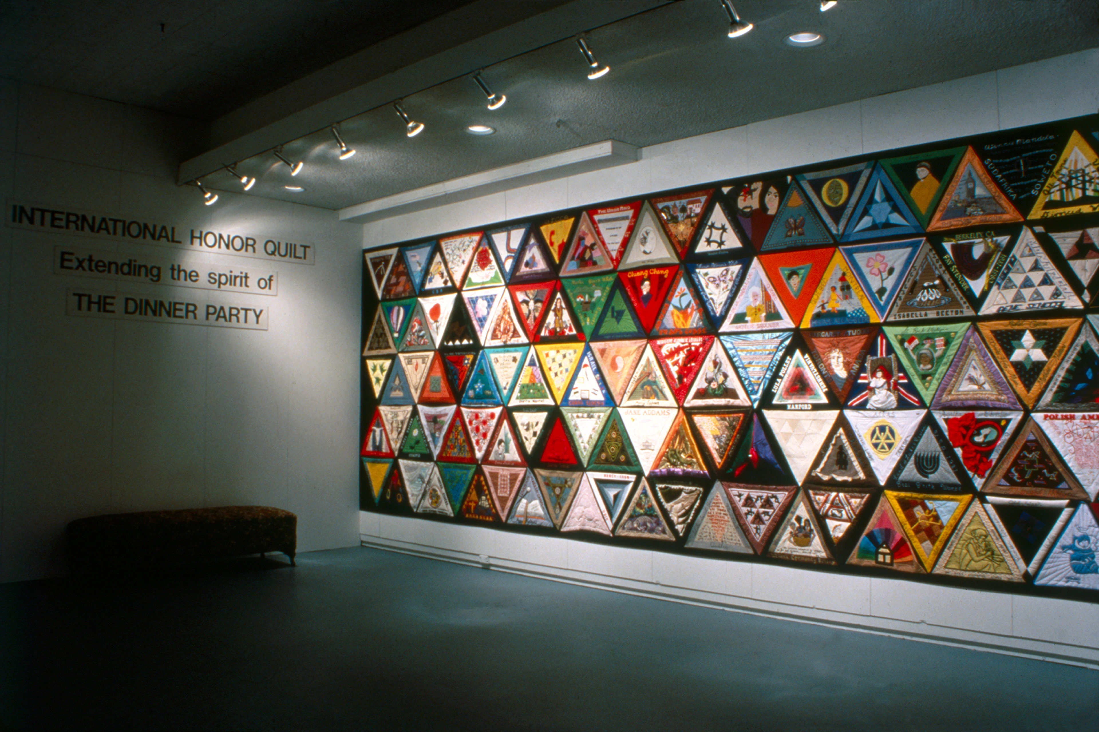 The International Honor Quilt, a large triangular quilt extending the spirit of Judy Chicago's The Dinner Party, displayed on a gallery wall.