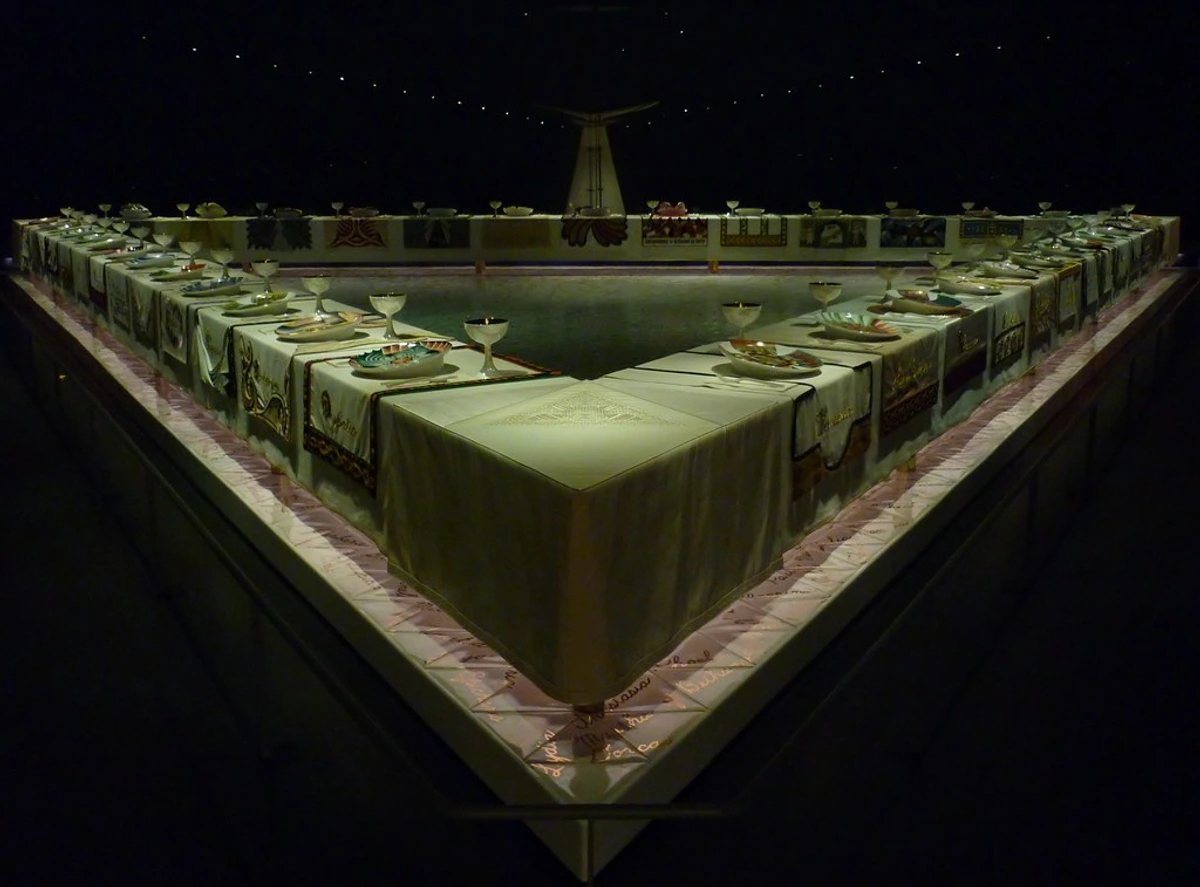 Judy Chicago's The Dinner Party installation at the Brooklyn Museum, featuring a triangular table with elaborate place settings.