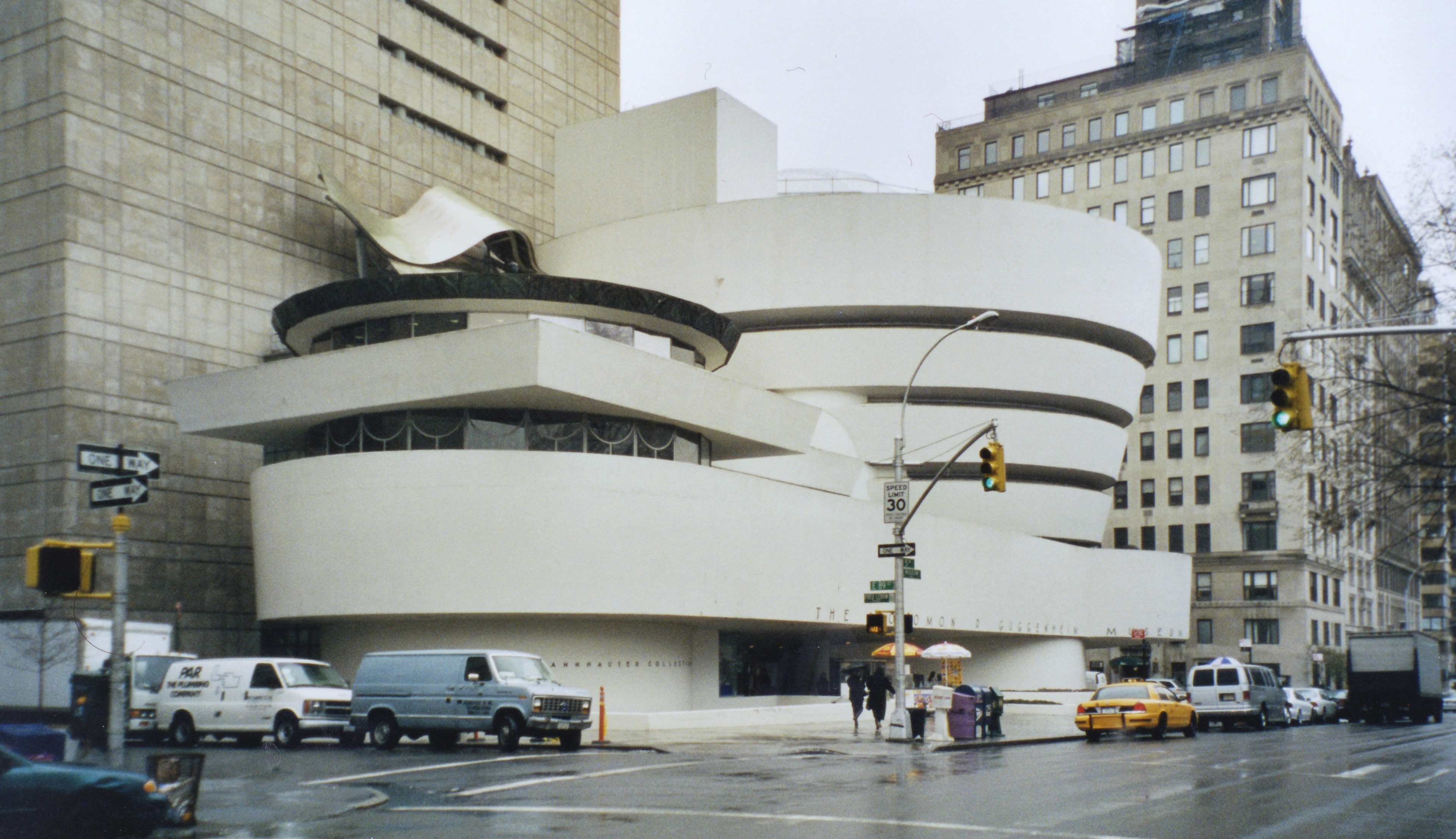 The iconic Guggenheim Museum in New York City, designed by Frank Lloyd Wright, on a rainy day with traffic and pedestrians.