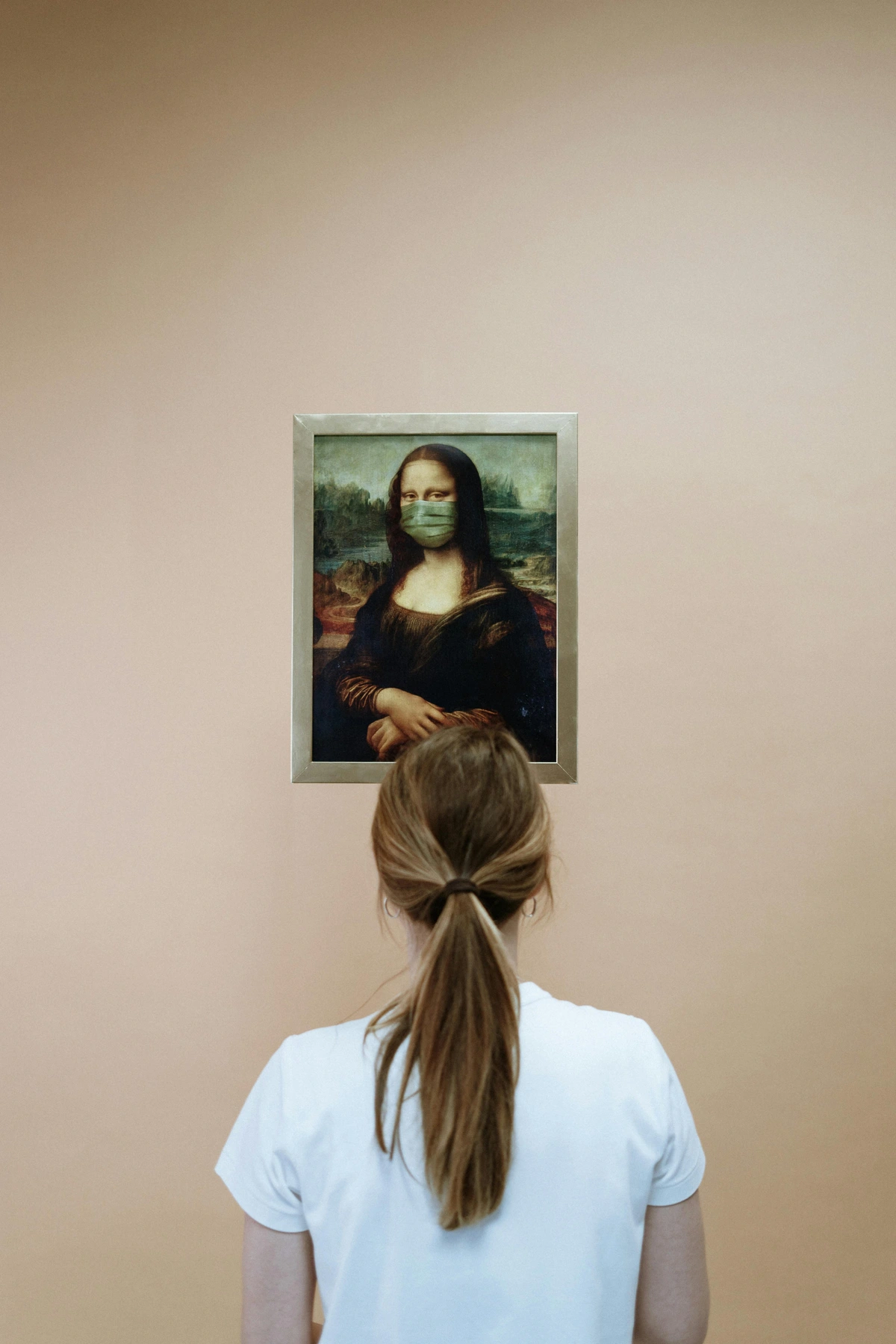 Woman in white shirt looking at a painting of the Mona Lisa wearing a face mask.