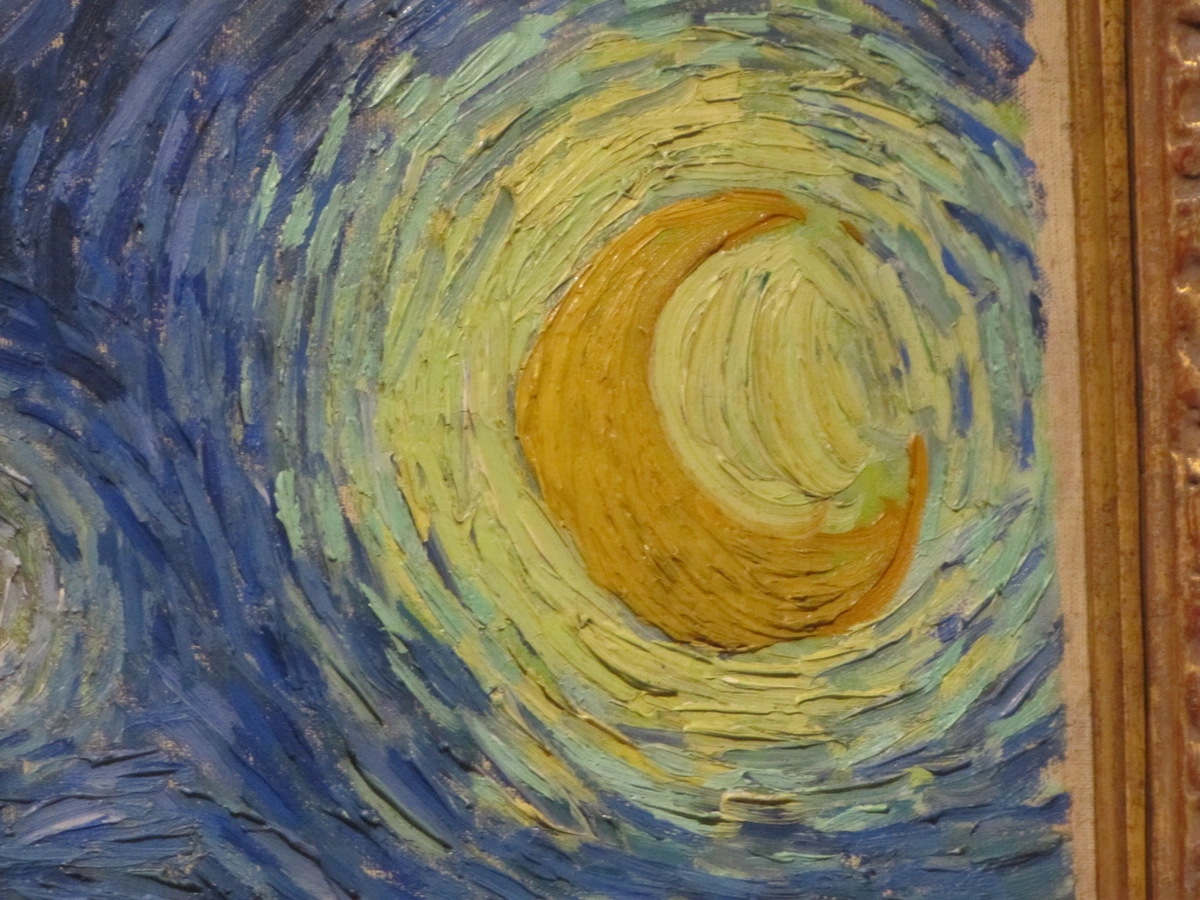 Close-up of Van Gogh's Starry Night painting showing the crescent moon and swirling sky