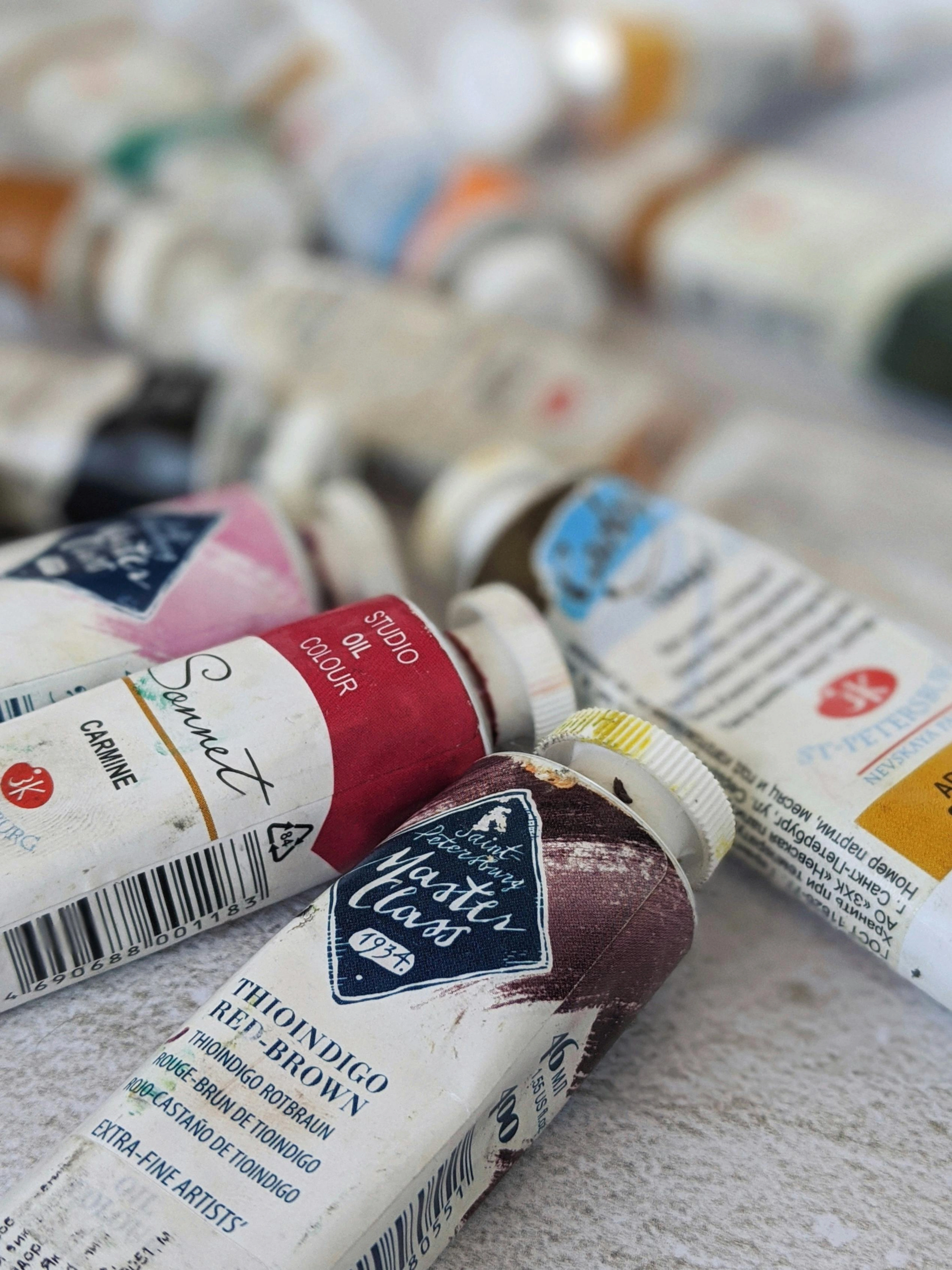 Close-up of various oil paint tubes, including brands like Master Class and Sonnet, with colors like Carmine and Thioindigo Red-Brown.
