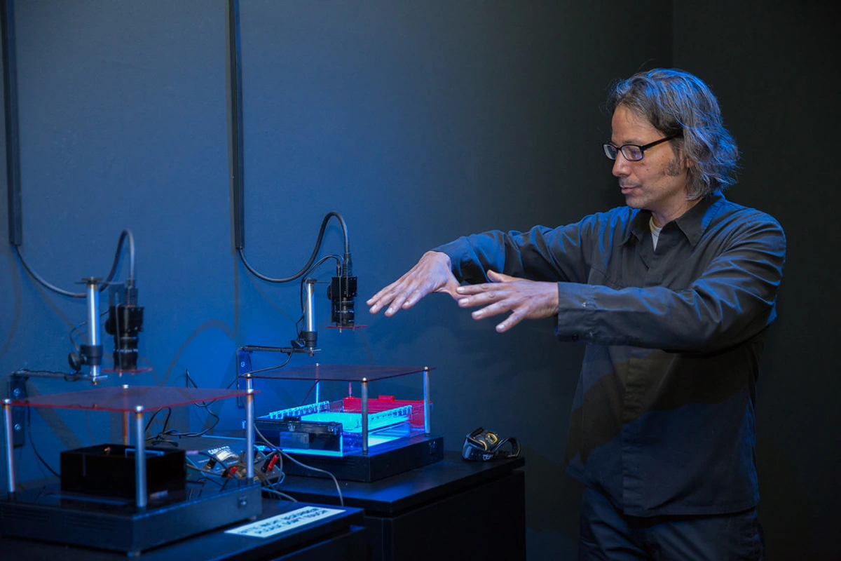 Paul Vanouse demonstreert bio-kunstinstallatie met microscoop en petrischalen