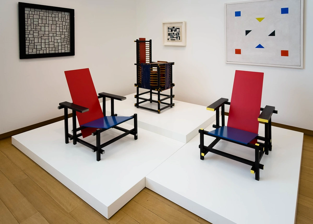 De Stijl exhibition at Stedelijk Museum Amsterdam featuring Gerrit Rietveld's iconic Red and Blue Chair and abstract paintings.