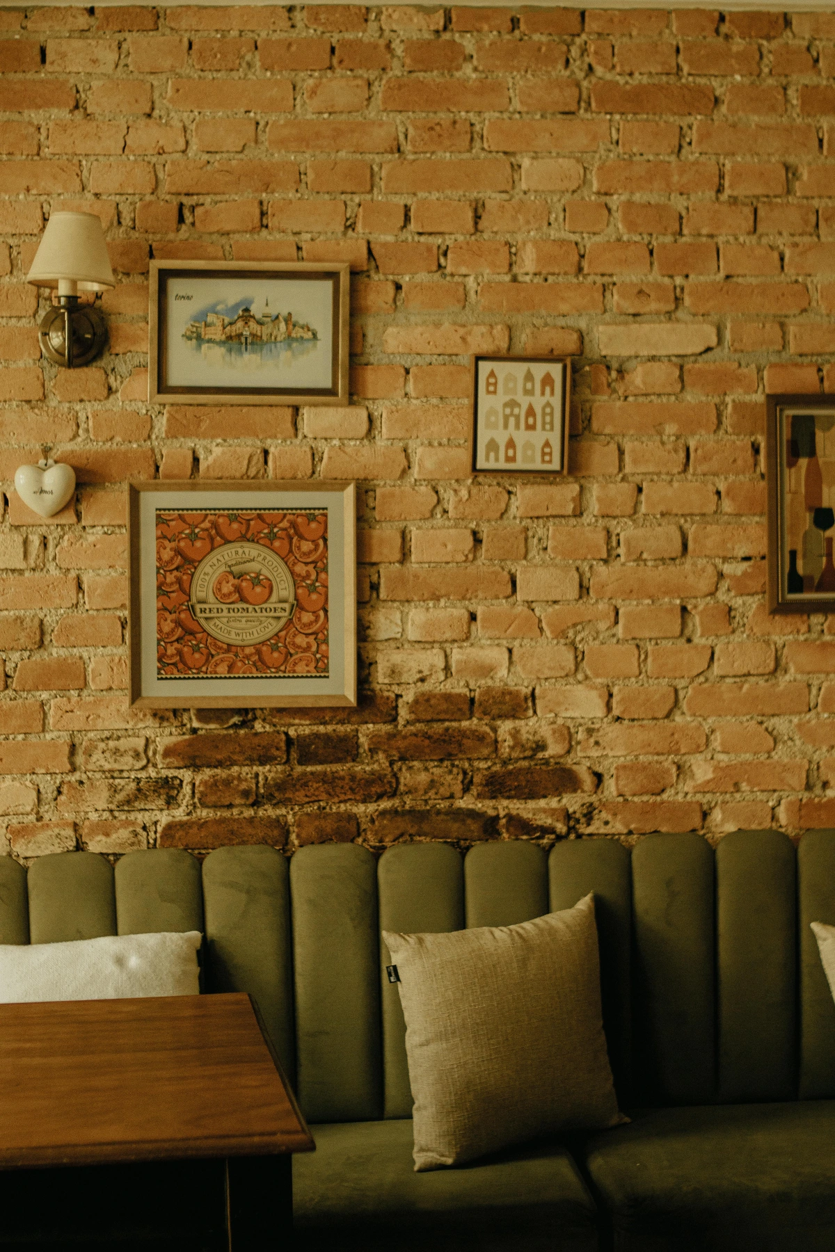 Cozy vintage cafe interior with a green velvet sofa, wooden table, and brick wall decorated with framed art and a heart-shaped ornament.