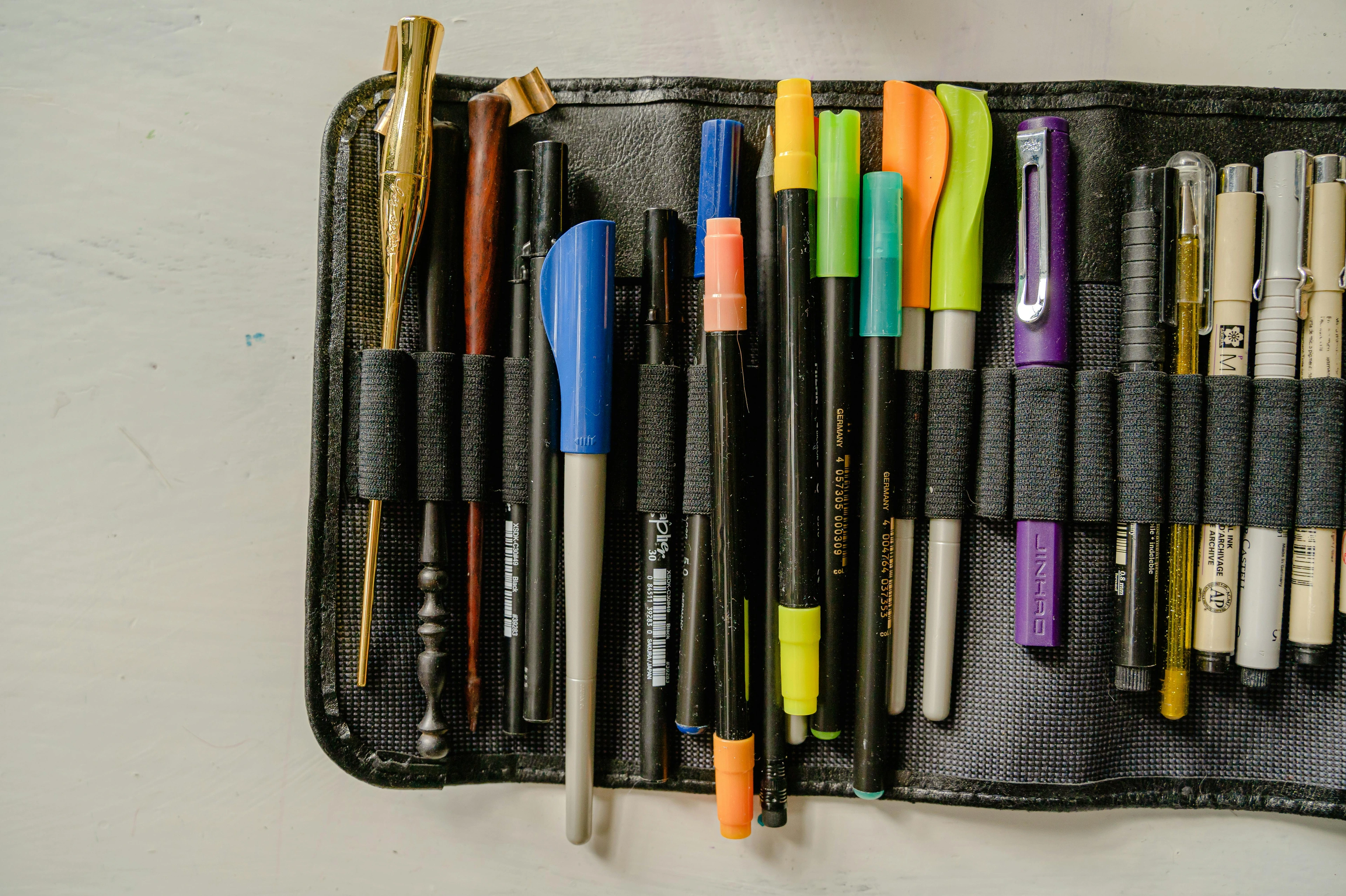 A collection of colorful pens and calligraphy tools neatly organized in a black case, showcasing a variety of writing instruments.