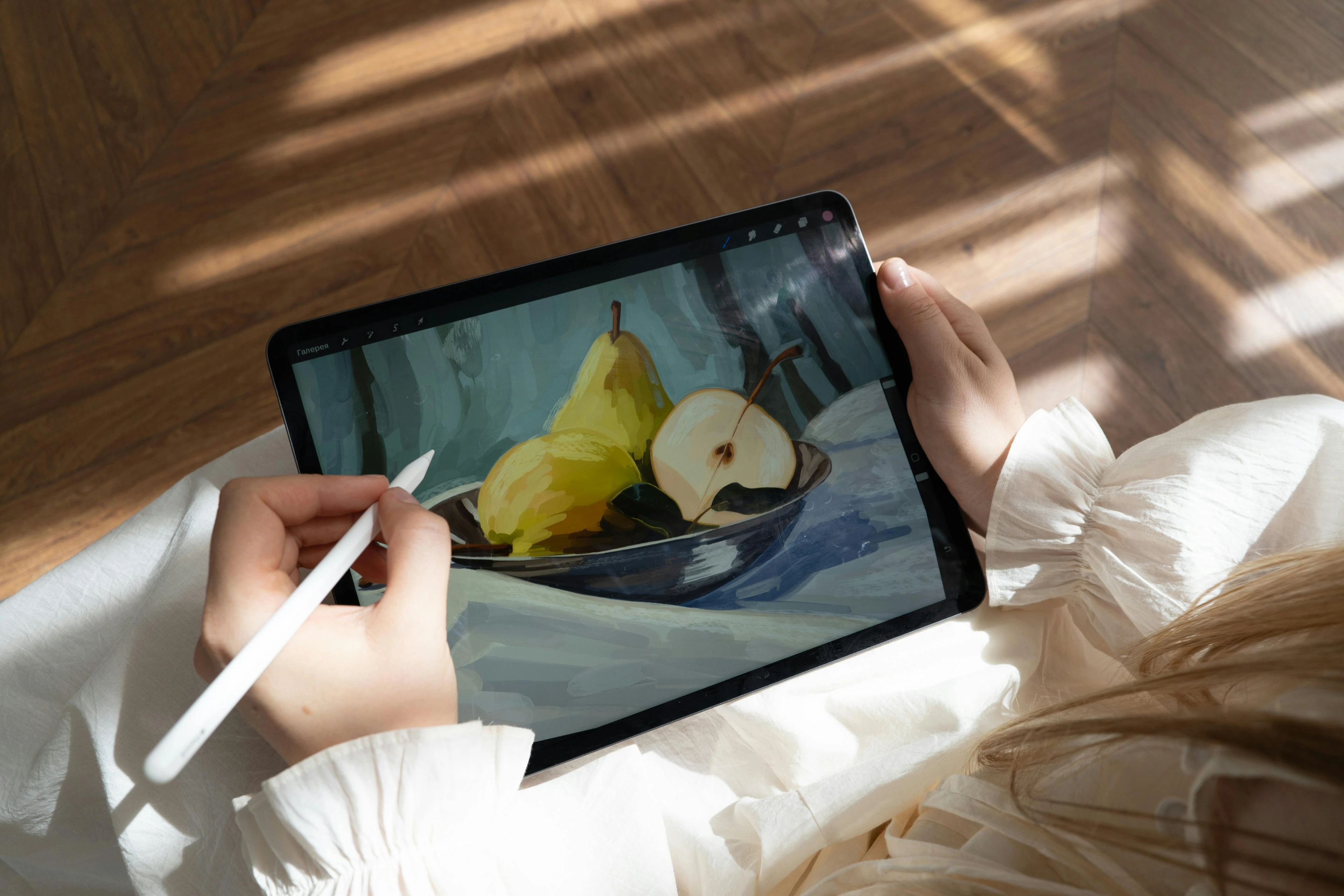 A person sketching on an an Apple iPad Pro with an Apple Pencil, displaying a digital painting of pears in a bowl.