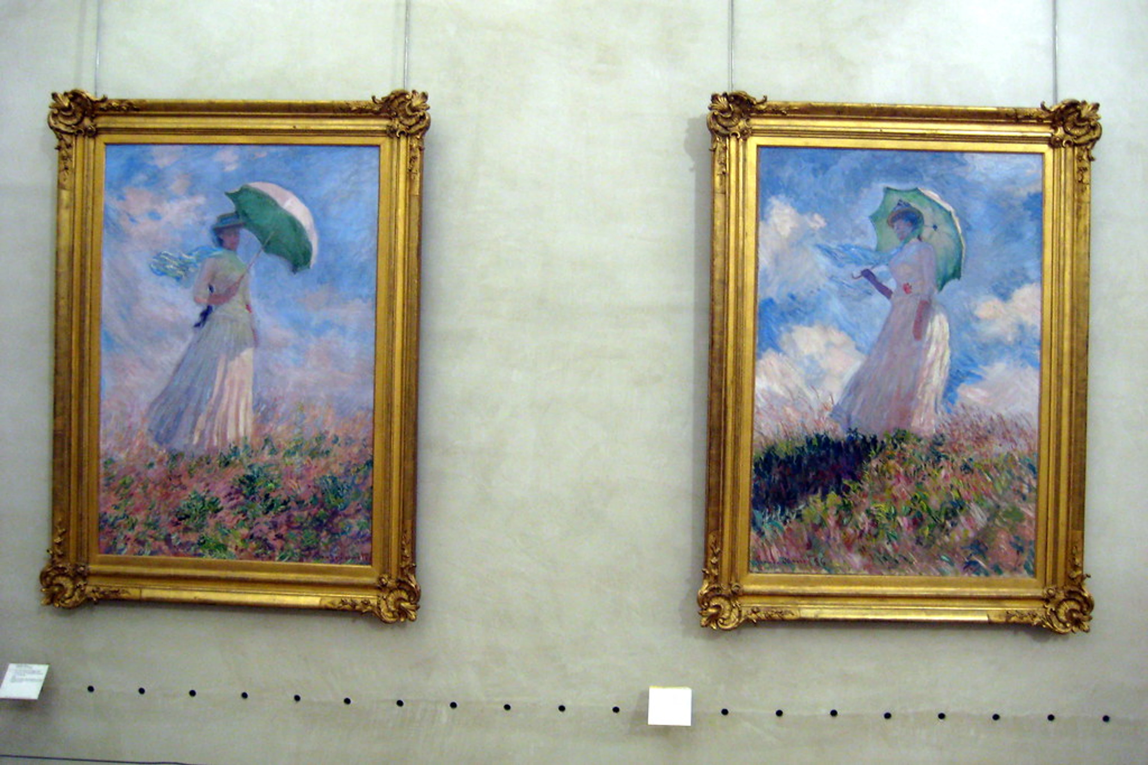 Two paintings by Claude Monet of women with umbrellas in a field, displayed in a museum.