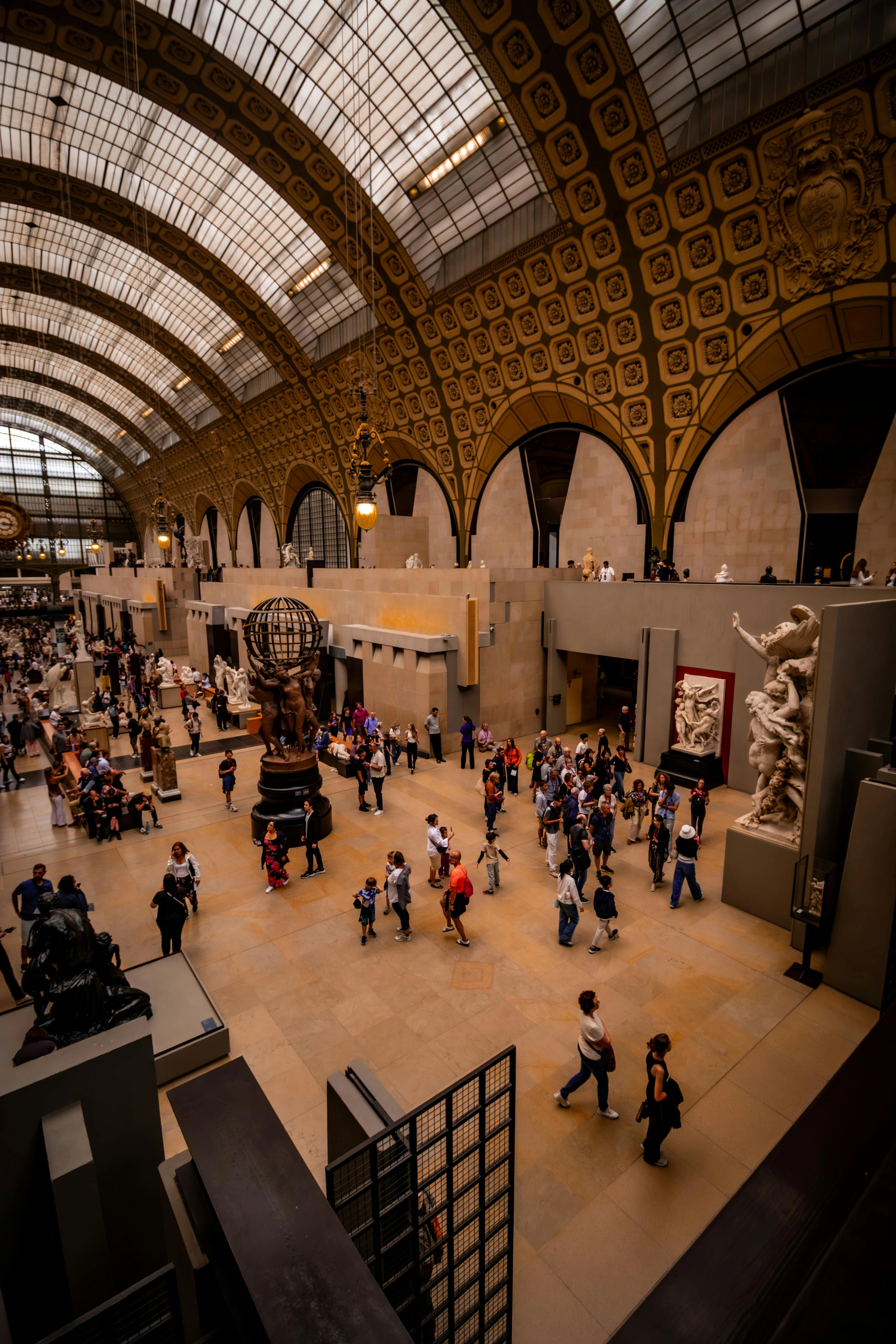 Visitors exploring the grand hall of the Musée d'Orsay in Paris, admiring sculptures and architecture under a glass ceiling.