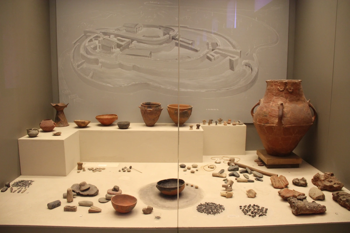 Display of ancient Greek Neolithic pottery and stone artifacts, including various vessels and tools, presented in a museum exhibit.