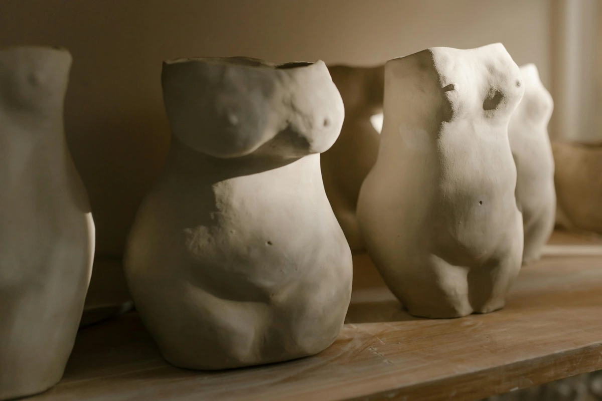 Clay sculptures of women's torsos on a wooden shelf, showcasing ceramic art techniques.