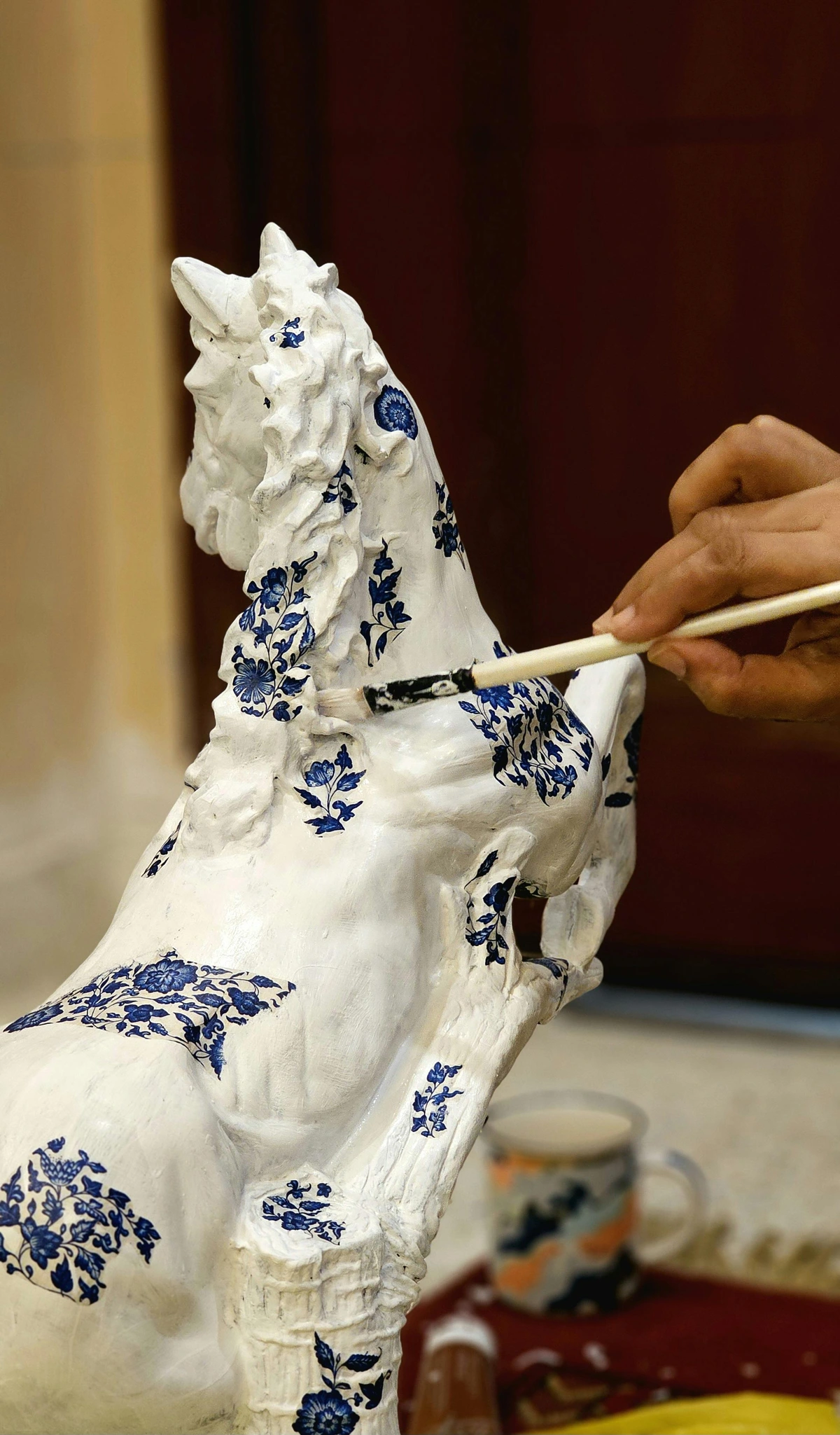 Craftsman painting a blue floral pattern onto a white ceramic horse statue
