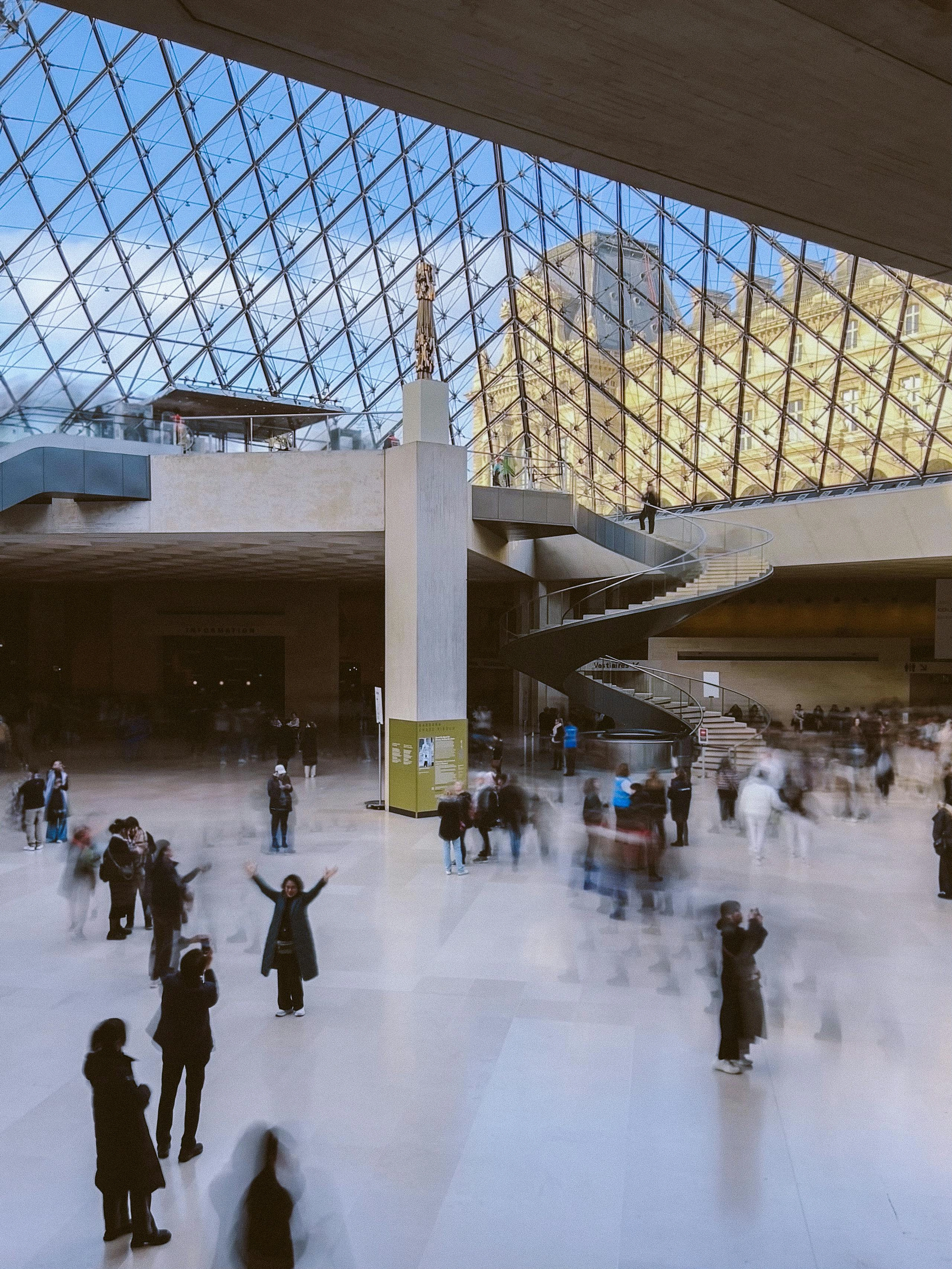 The bustling, modern interior of the Louvre Pyramid entrance, with natural light and visitors, serving as a gateway to the museum's collections.