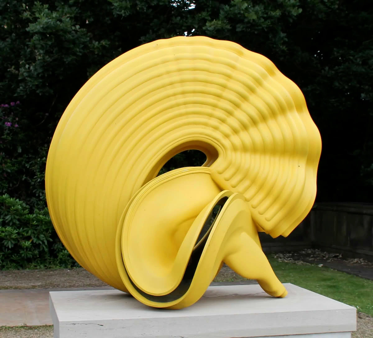 Tony Cragg's 'Pasta' sculptuur, een groot geel abstract kunstwerk met golvende richels, buiten tentoongesteld op een sokkel.