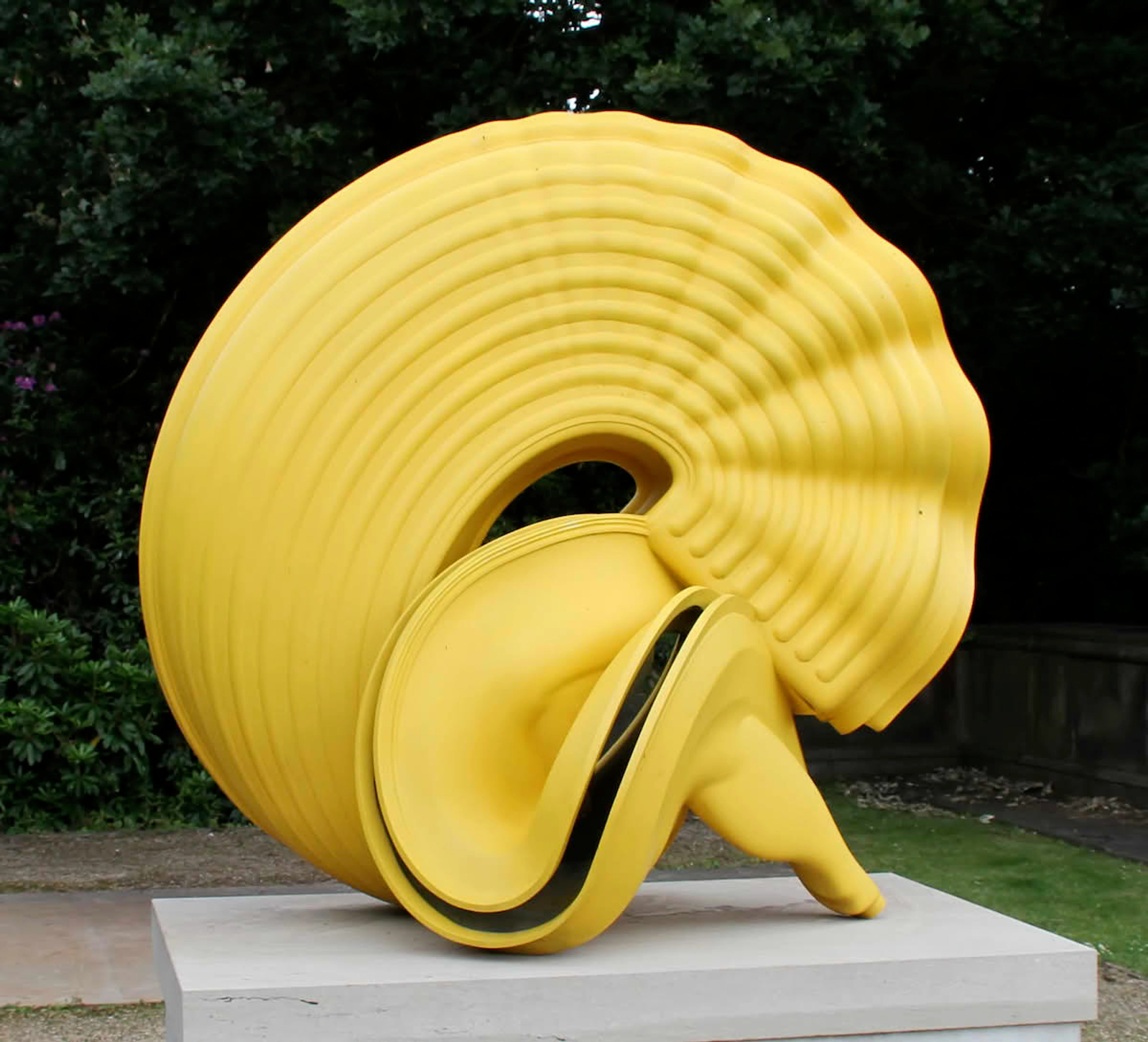 Tony Cragg's 'Pasta' sculpture, a large yellow abstract art piece with wavy ridges, displayed outdoors on a plinth.