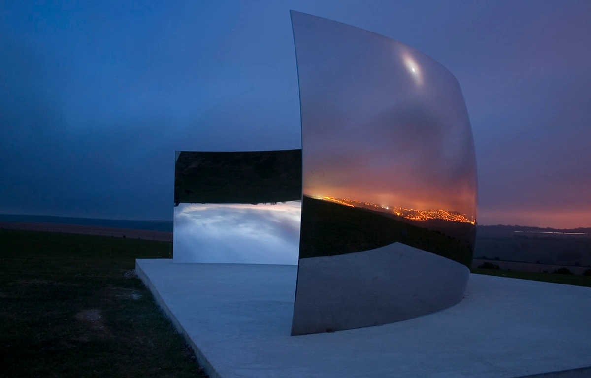 Anish Kapoor's C-Curve sculpture at dusk, reflecting the blue sky and distant city lights.