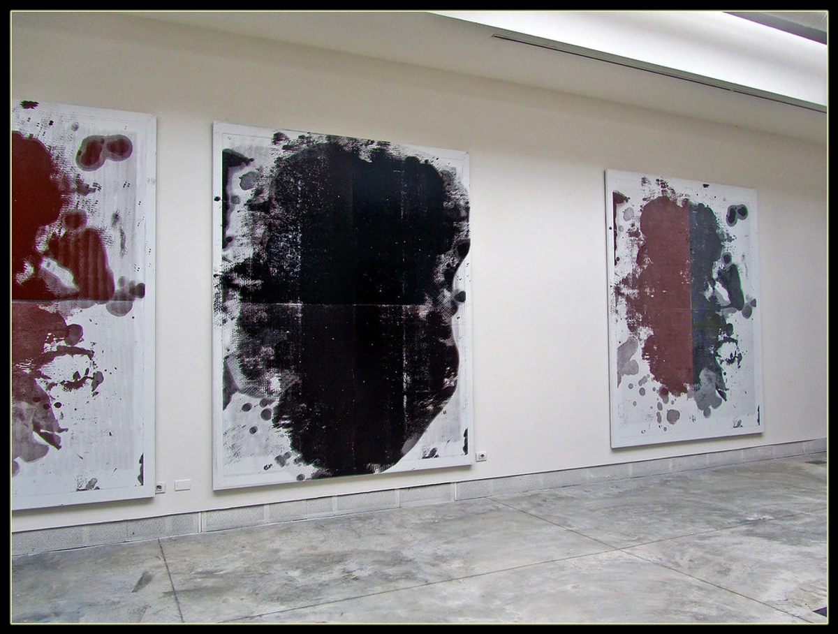 Three large abstract paintings by Christopher Wool, featuring black, dark red, and grey paint on white canvases, displayed in a modern art gallery.