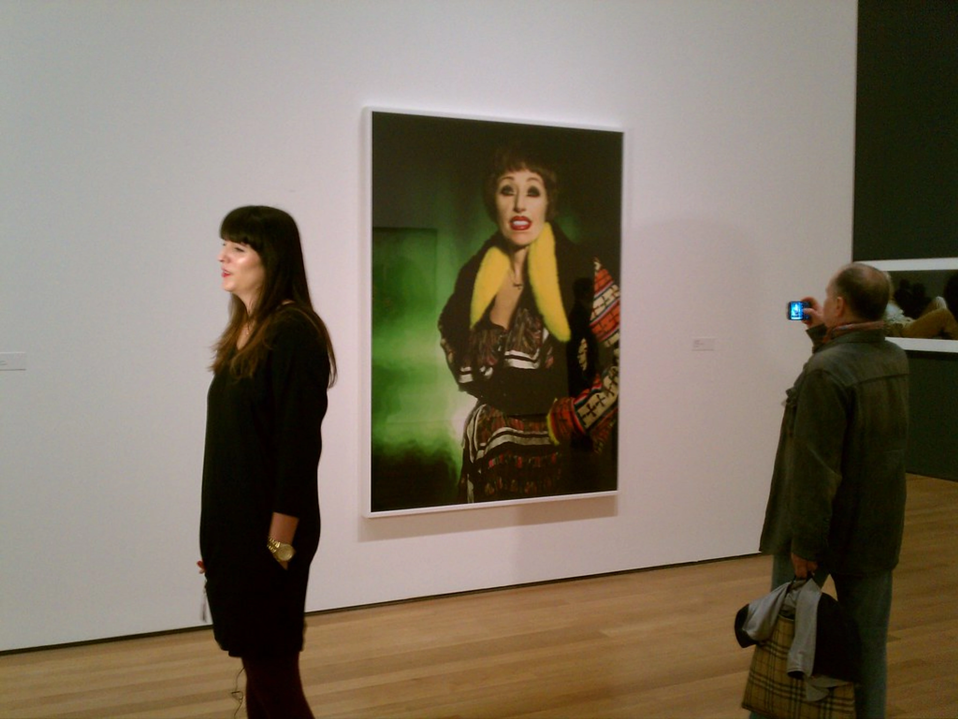 Visitors at the Cindy Sherman exhibition at MoMA, with one person photographing a large portrait by the artist.