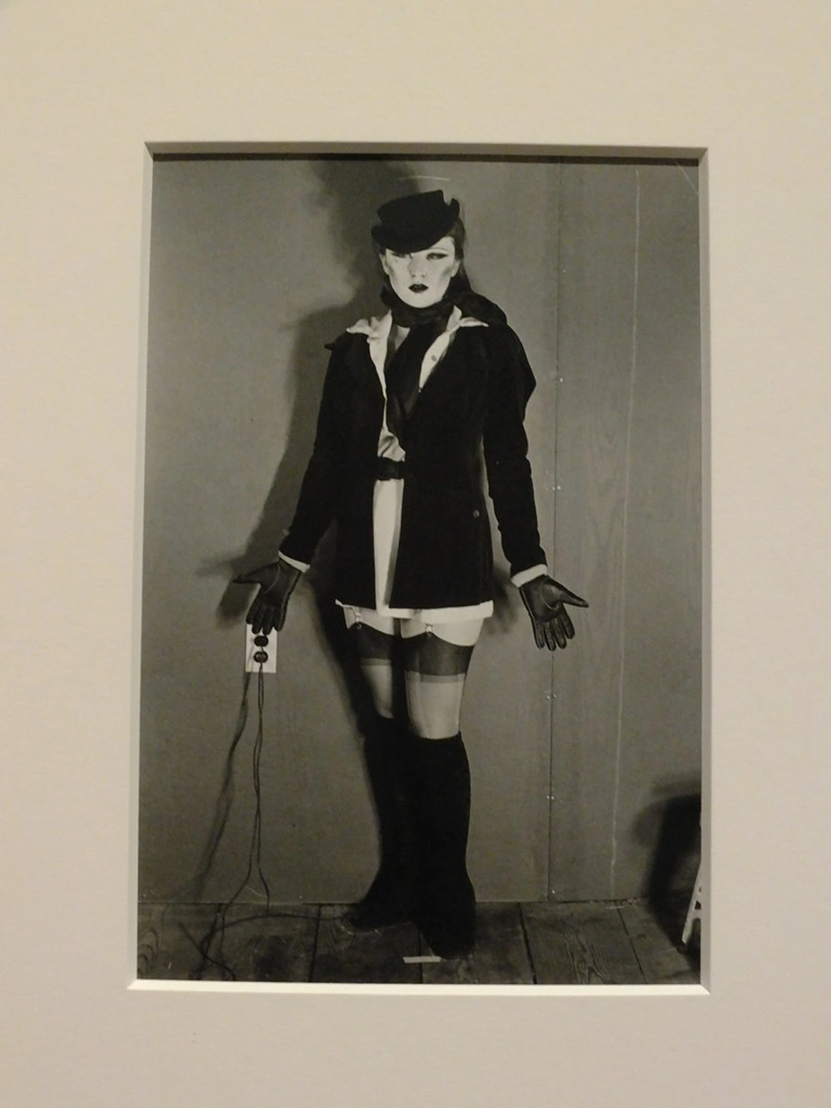 Cindy Shermans zwart-wit zelfportret uit haar Untitled (Line-Up) serie, waarop ze te zien is in een donkere jas, hoed en handschoenen, met een elektrische stekker.