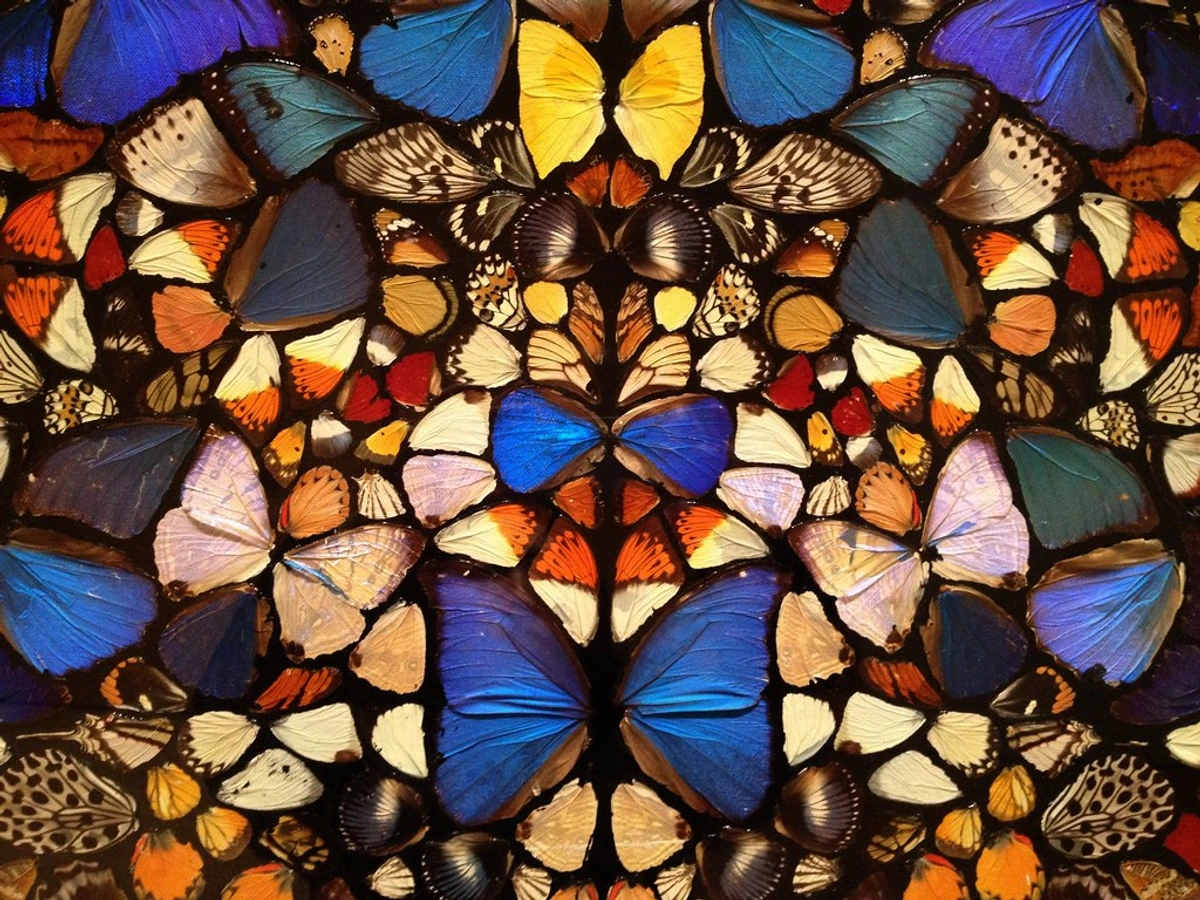 Damien Hirst's 'The Kingdom of the Father' artwork, a vibrant mosaic of colorful butterfly wings in blue, yellow, and orange hues.