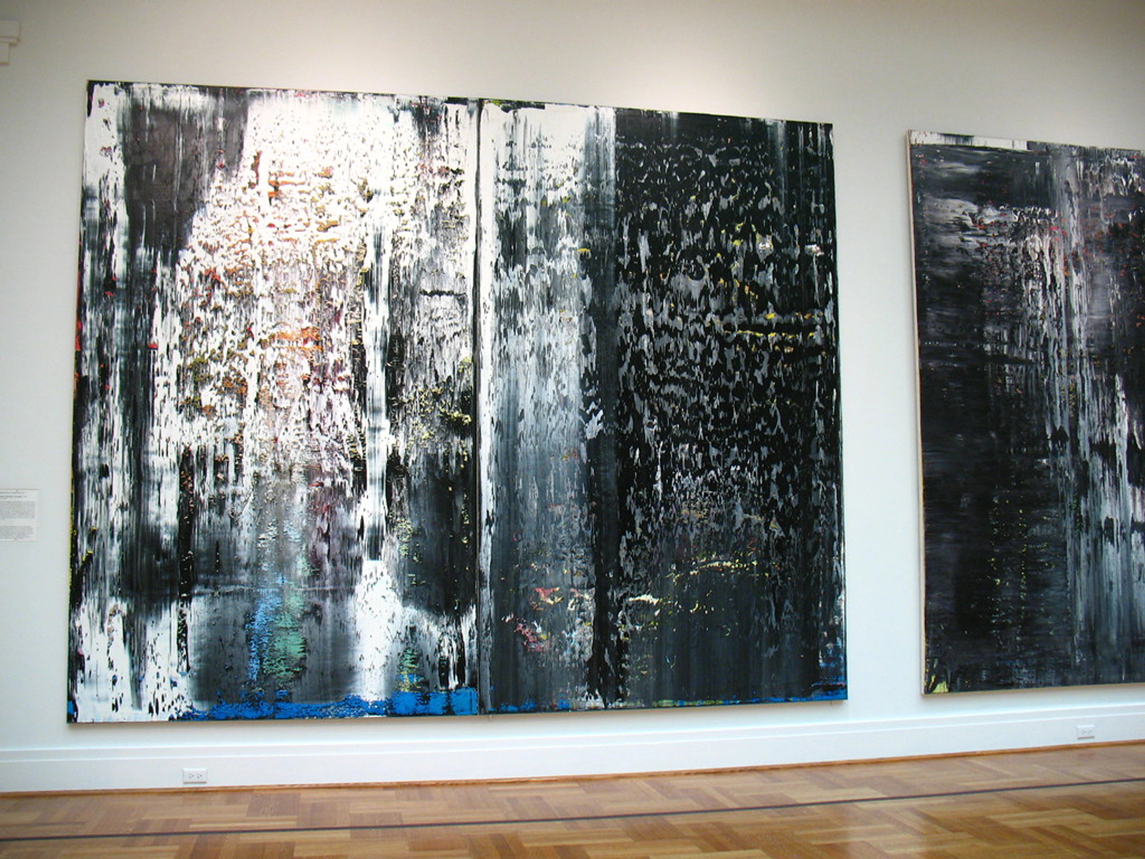 Two large abstract paintings by Gerhard Richter, titled 'January, December, November, 1989', featuring black, white, and grey vertical streaks with hints of color, displayed in a museum.