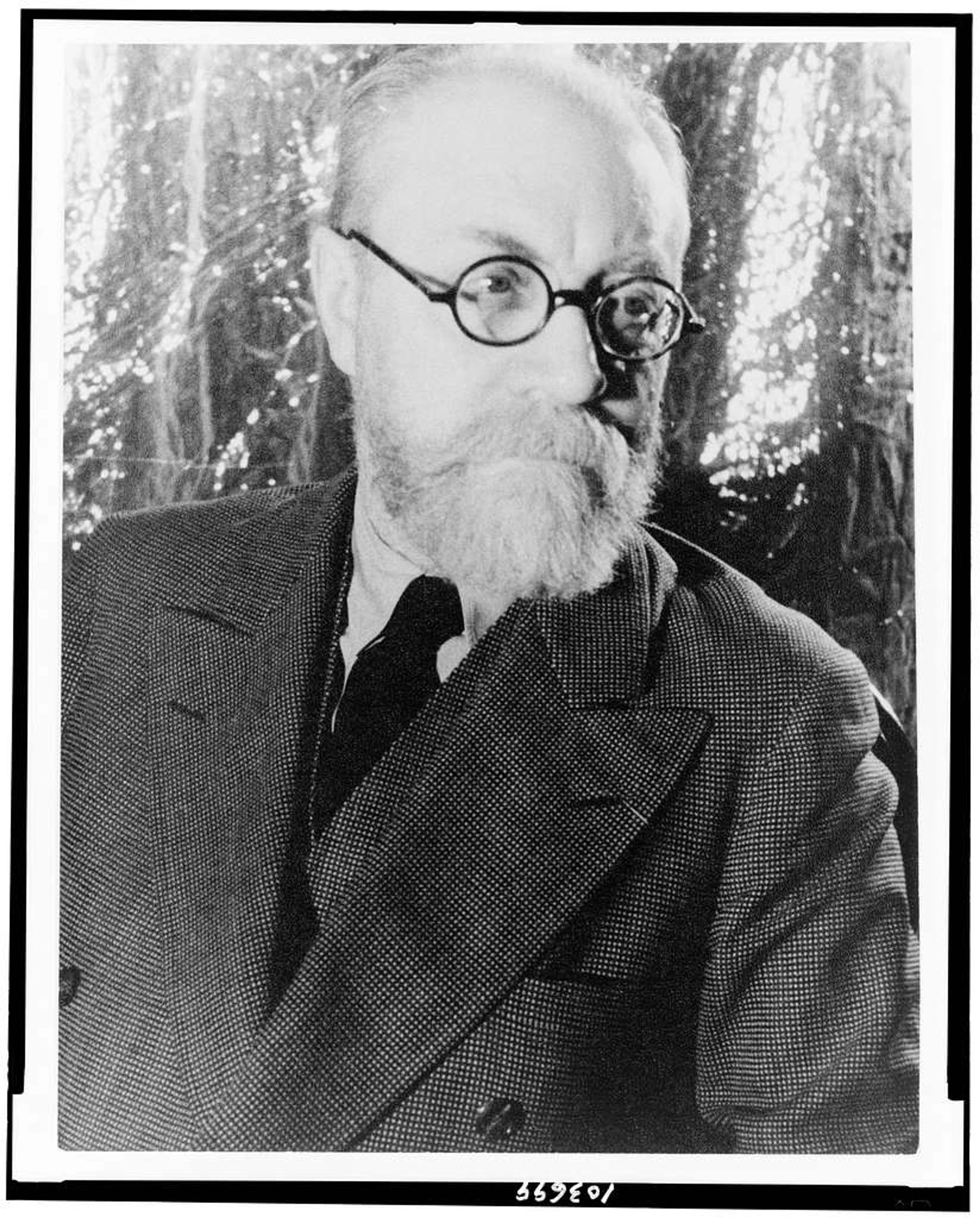 Black and white portrait of famous French artist Henri Matisse, an older man with a white beard and round glasses, wearing a suit and tie, looking slightly to the right.