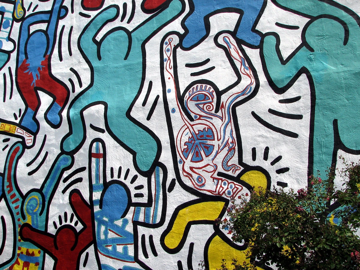 Close-up of Keith Haring's 'We The Youth' mural, featuring vibrant dancing figures in blue, red, and turquoise on a white background.