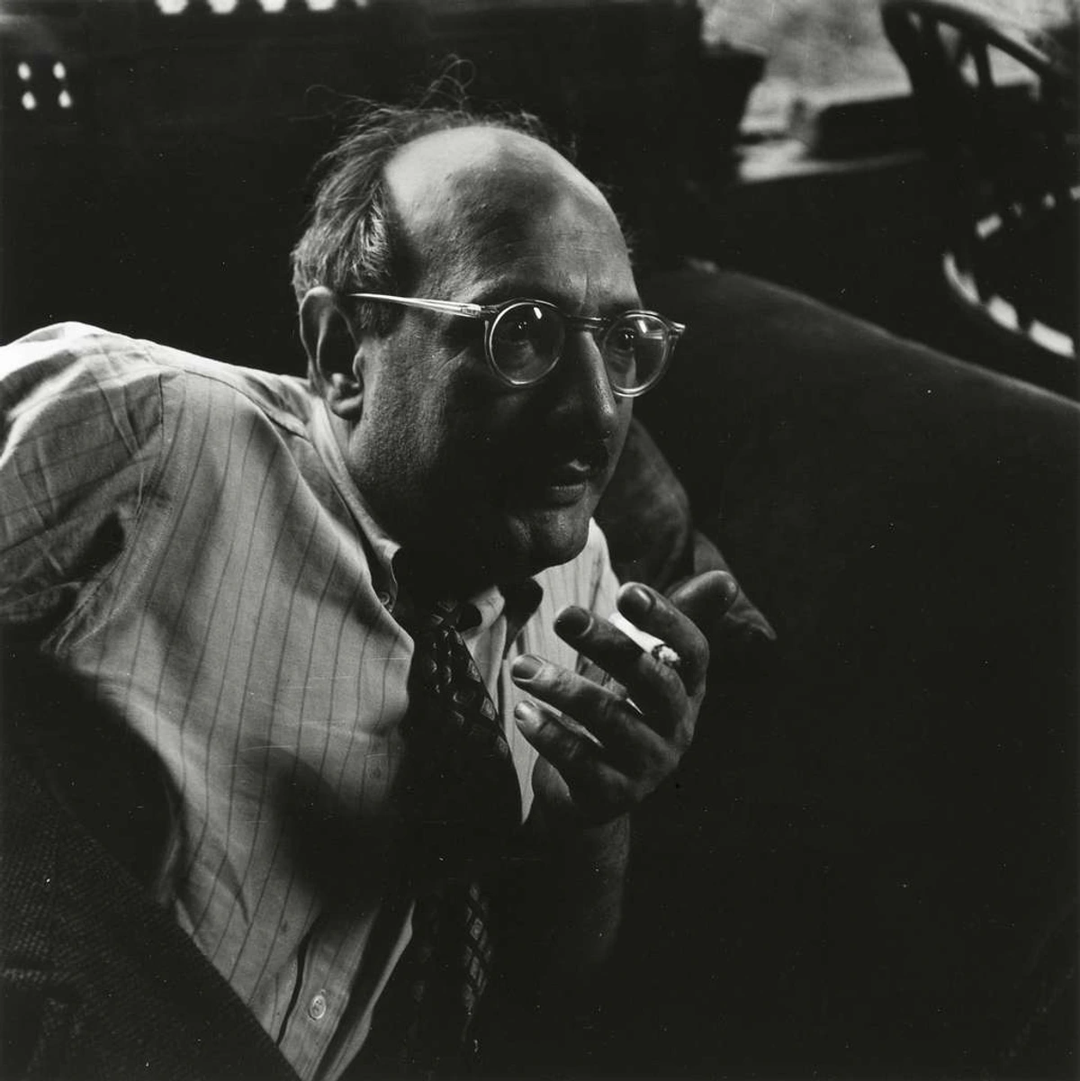 Black and white portrait of Mark Rothko in glasses, wearing a striped shirt and tie, holding a cigarette in his hand.